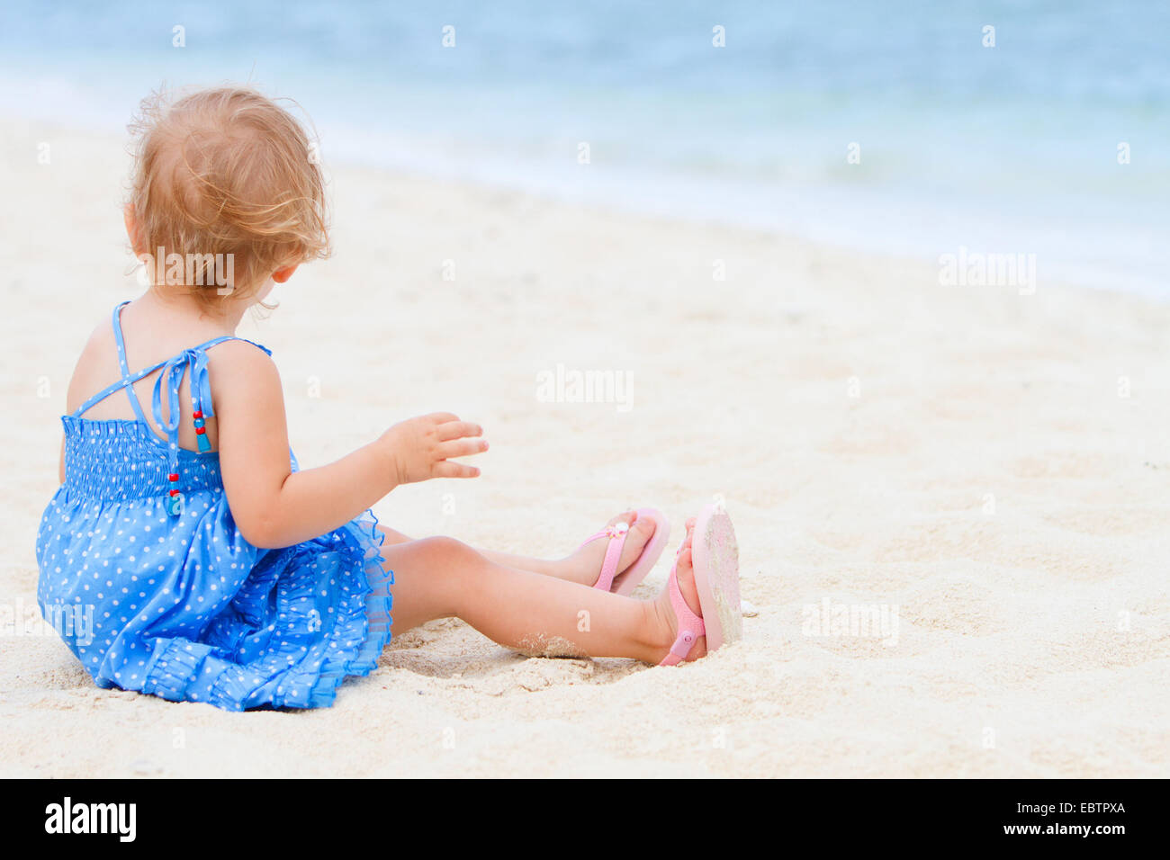 Il toddler ragazza seduta sulla sabbiosa spiaggia tropicale Foto Stock