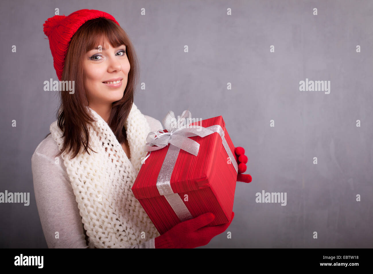 Giovane donna nel cappuccio rosso e guanti mantiene il regalo di Natale avvolto in carta rossa, Foto Stock