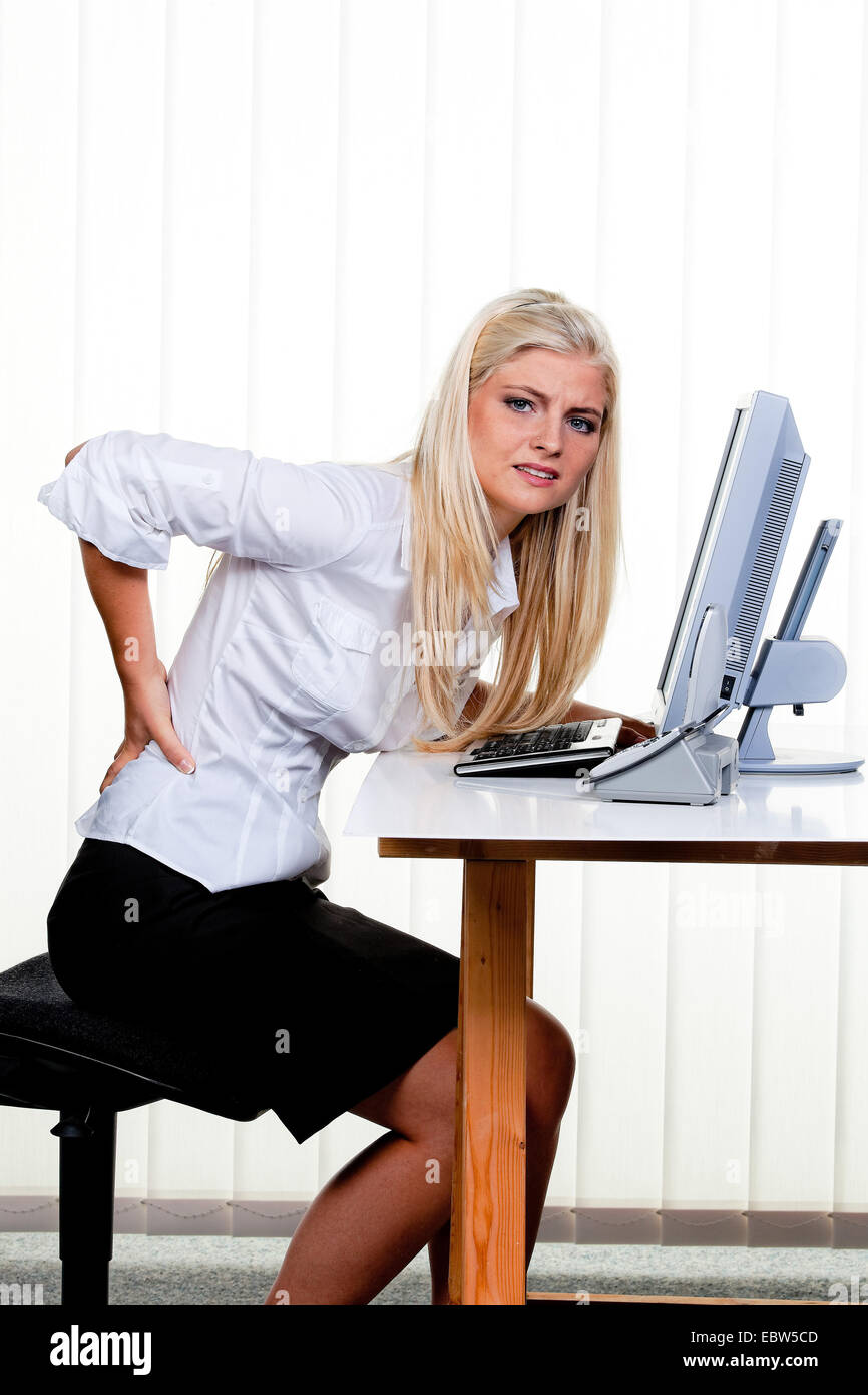 Giovane donna con il mal di schiena in ufficio Foto Stock