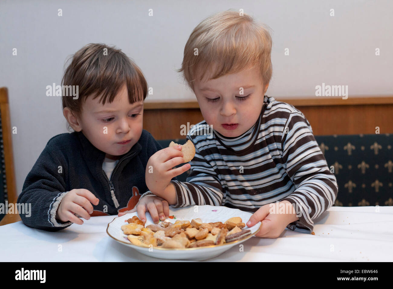Due ragazzini seduti al tavolo della cucina sostenendo circa biscotti di Natale su una piastra Foto Stock