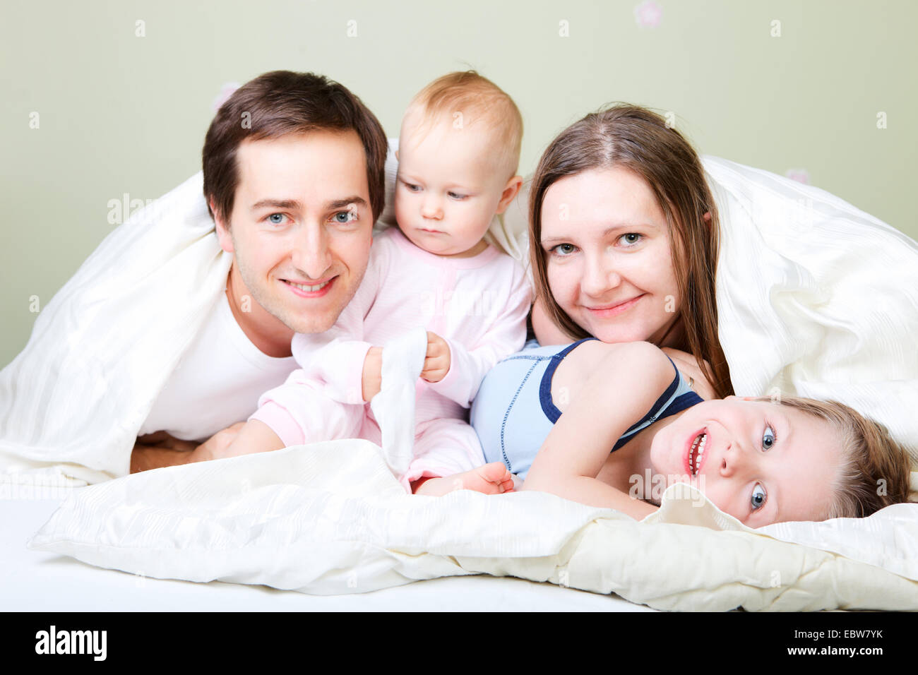 Giovane famiglia con due bambini piccoli sdraiati a letto Foto Stock