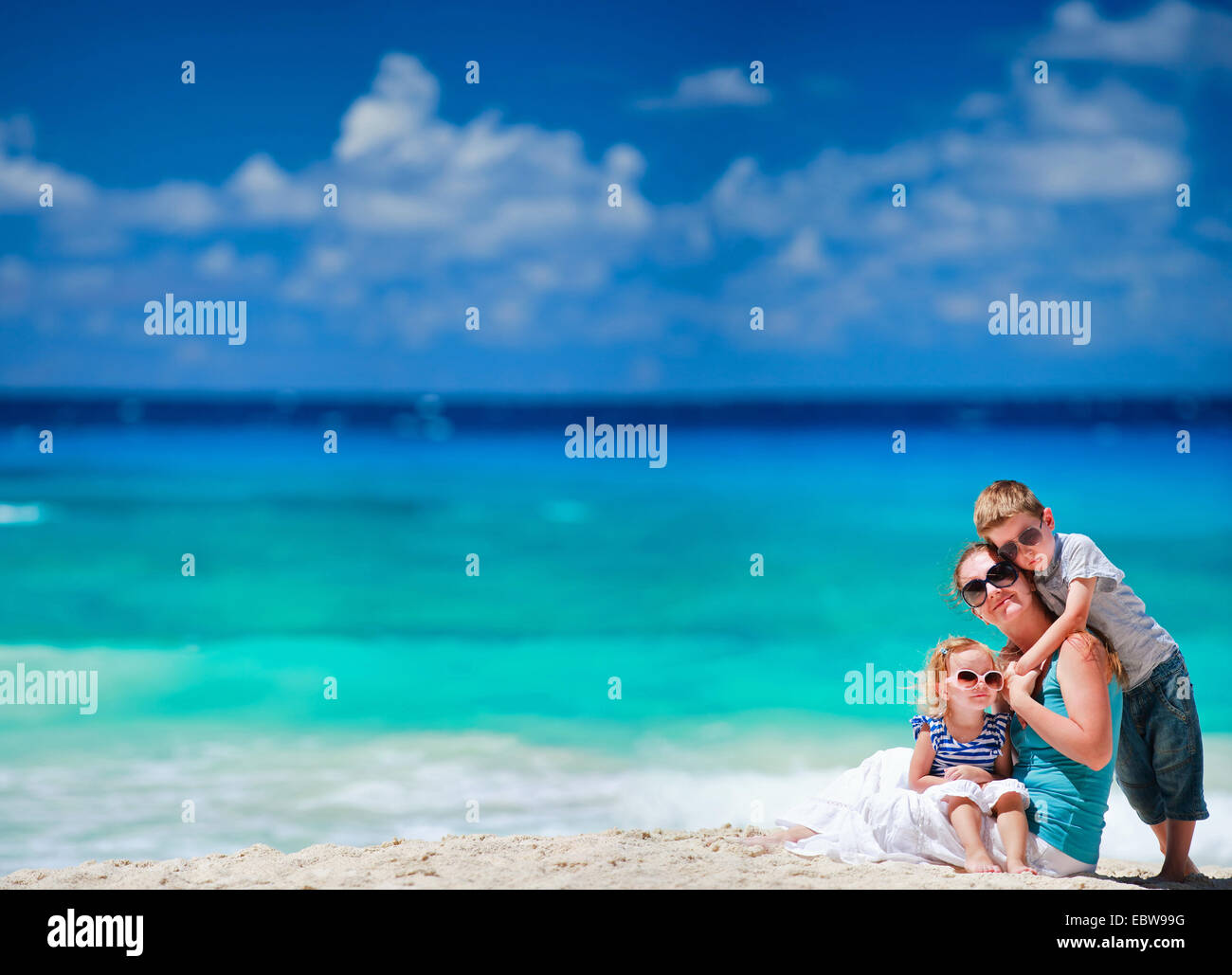 Giovane madre e figlia seduti sulla spiaggia sabbiosa e suo figlio che abbraccia il suo Foto Stock