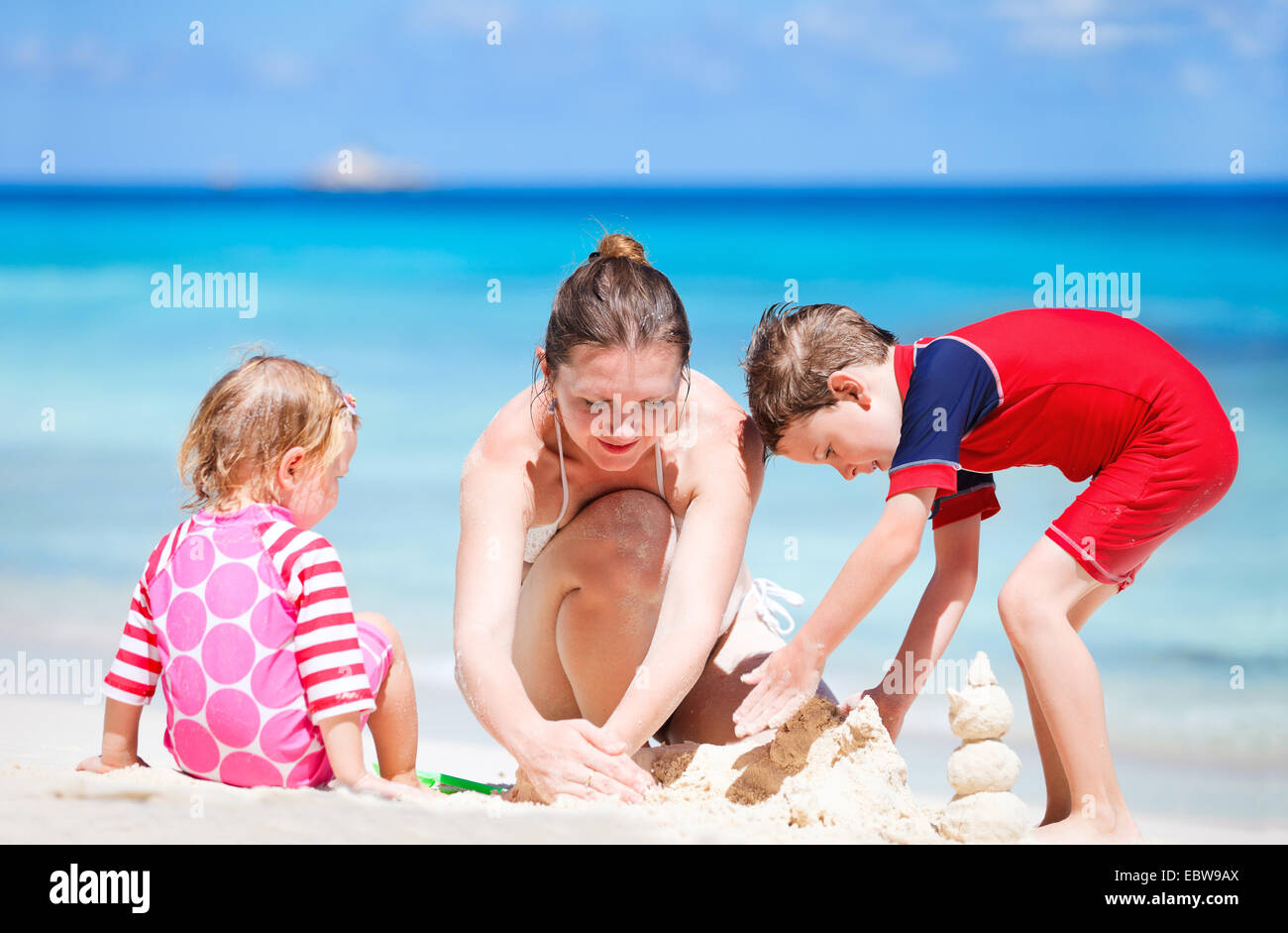 Una giovane madre e i suoi due figli la costruzione di un castello di sabbia sulla spiaggia di sabbia Foto Stock