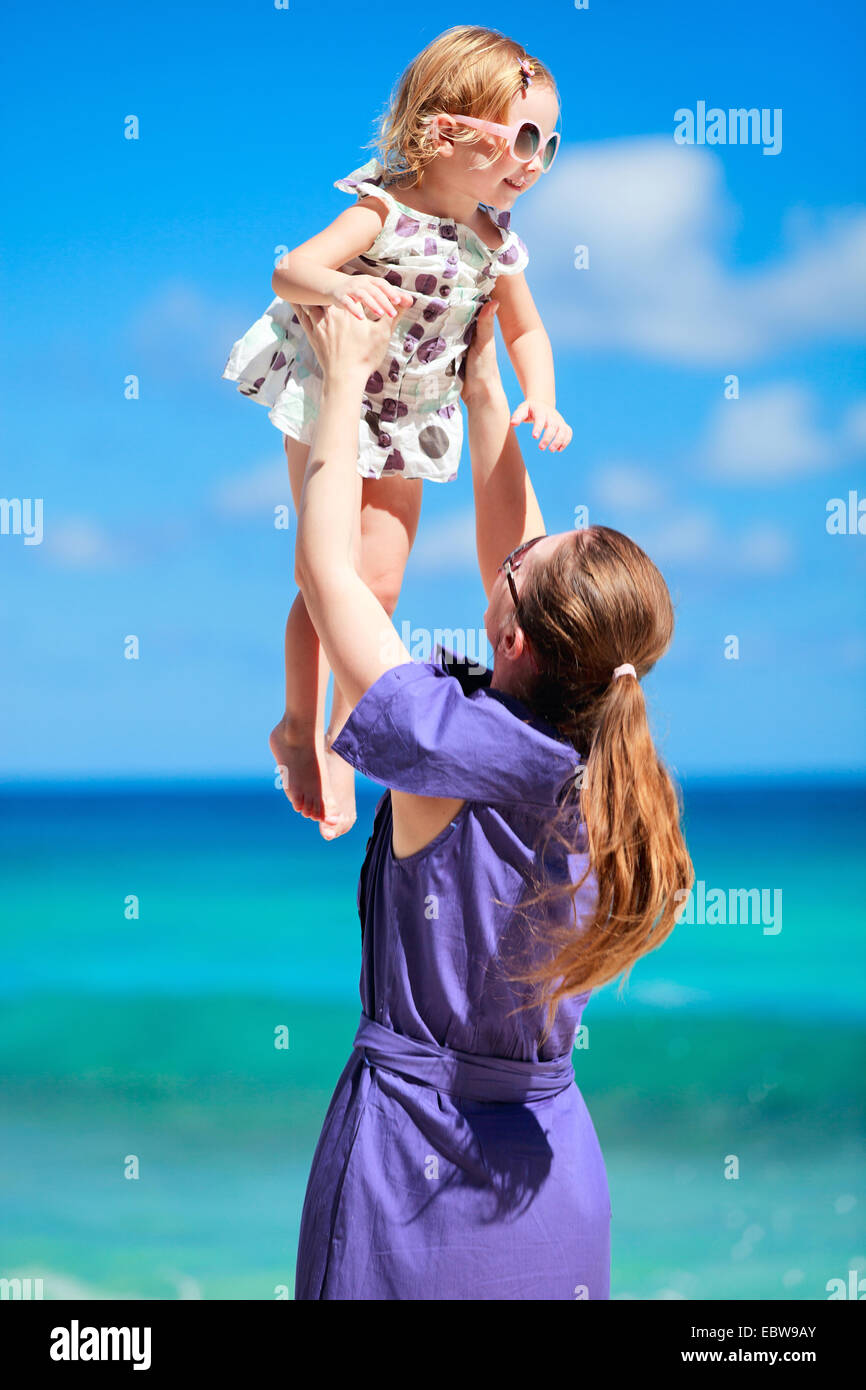 Una giovane madre solleva la sua piccola figlia sulla spiaggia tropicale Foto Stock