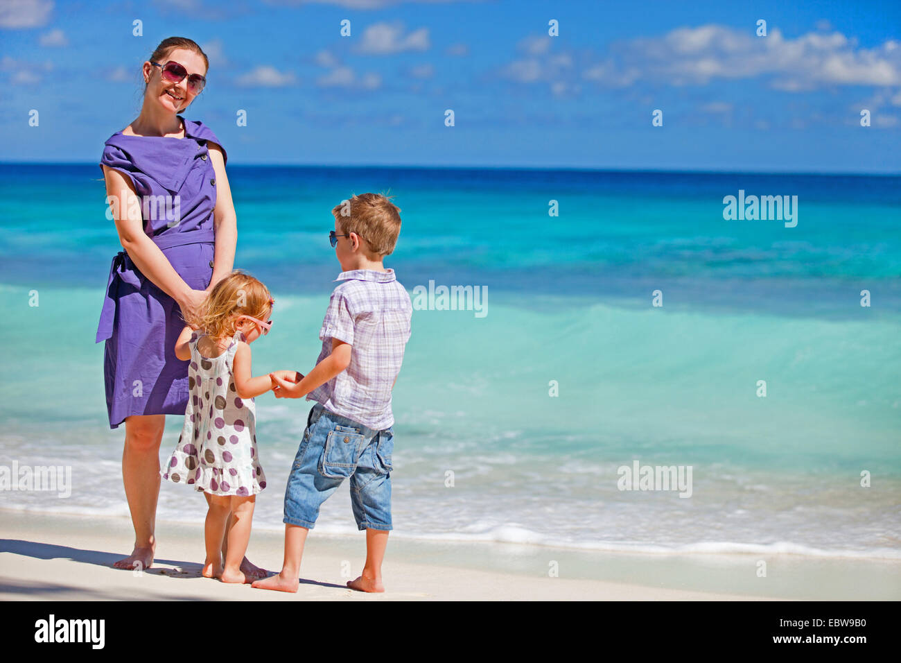 Una giovane madre in piedi con la sua piccola bambini sulla spiaggia tropicale Foto Stock