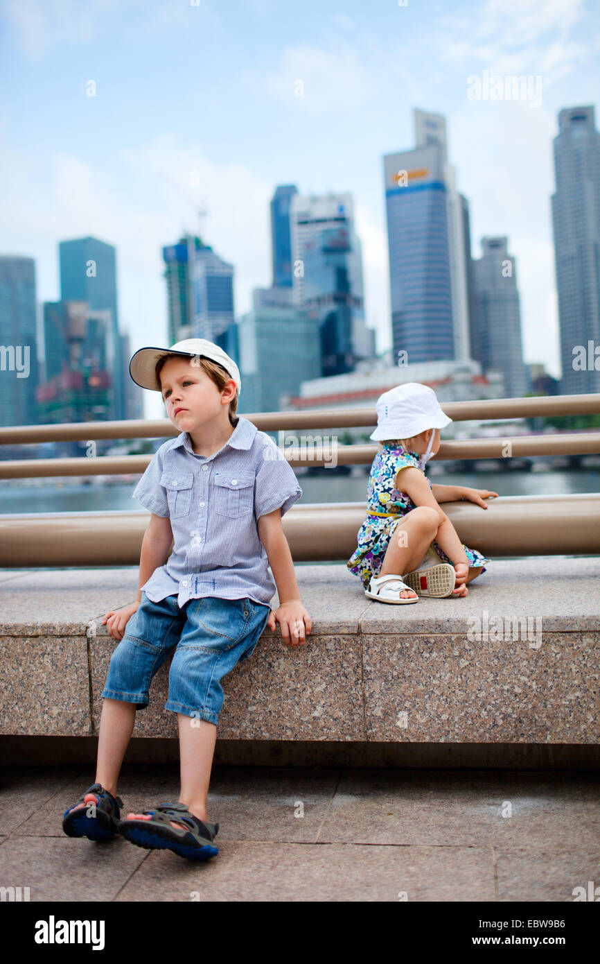 Due piccoli bambini seduti nel centro città, Singapore, Singapore Foto Stock