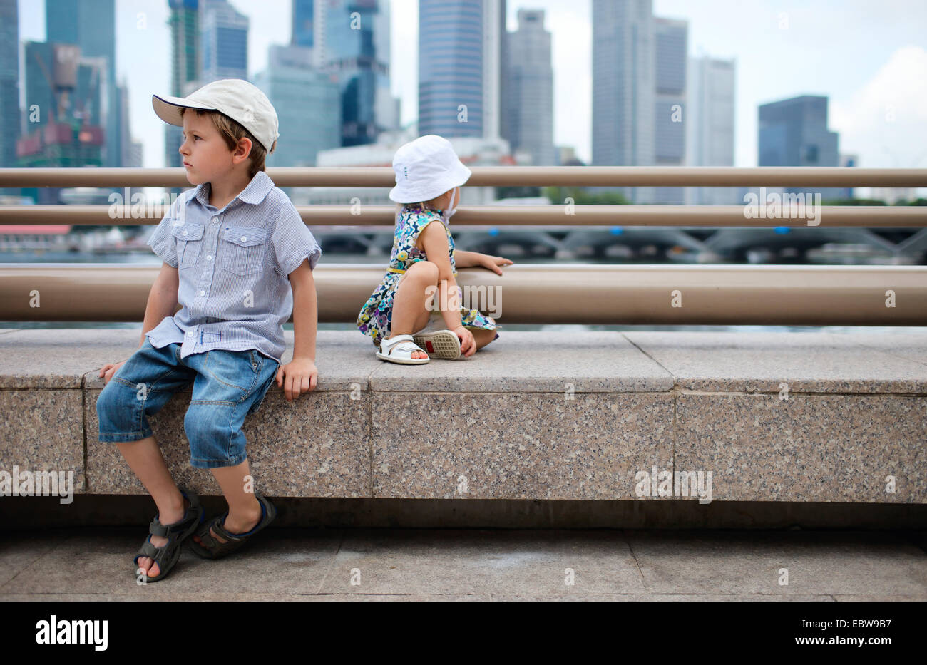 Due piccoli bambini seduti nel centro città, Singapore, Singapore Foto Stock
