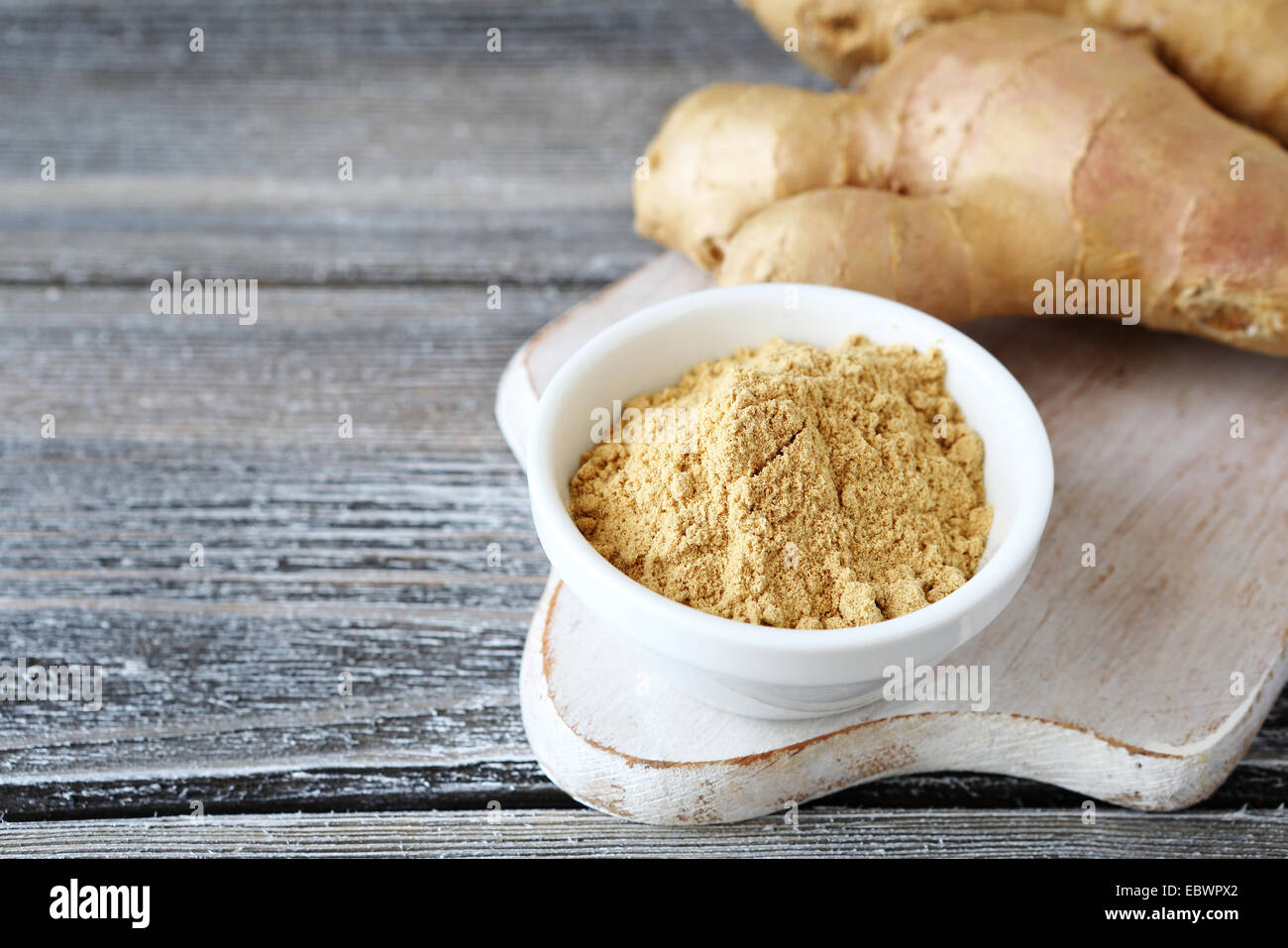 Di zenzero fresco con una piccante in polvere nella ciotola, sullo sfondo di legno Foto Stock