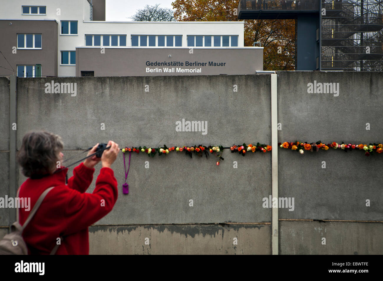 Donna di prendere una fotografia di fiori posti nel muro di Berlino durante il venticinquesimo anniversario della sua caduta Foto Stock