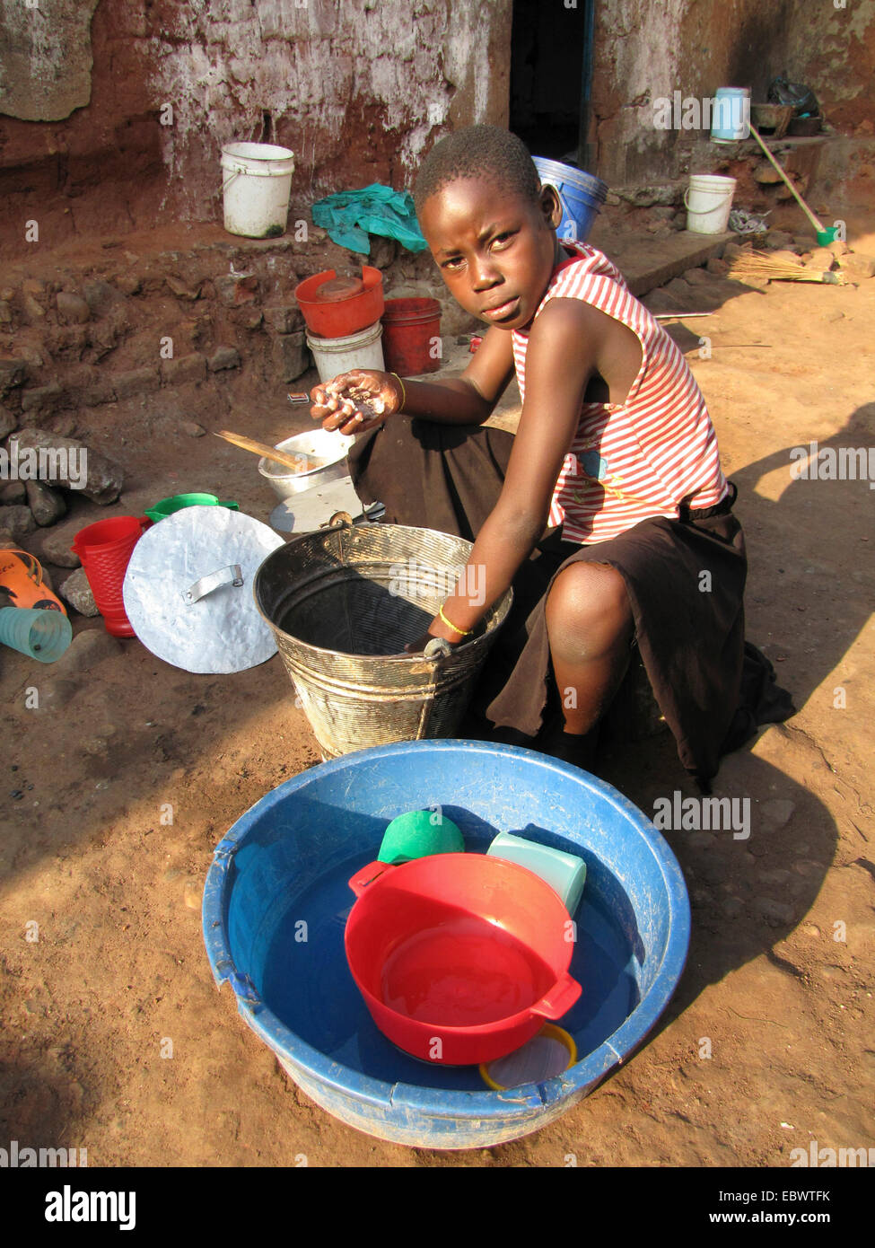 Ragazza di lavaggio piatti primitivo sul suolo di terra di un cortile, Burundi, Bujumbura mairie, Bwiza Bujumbura Foto Stock