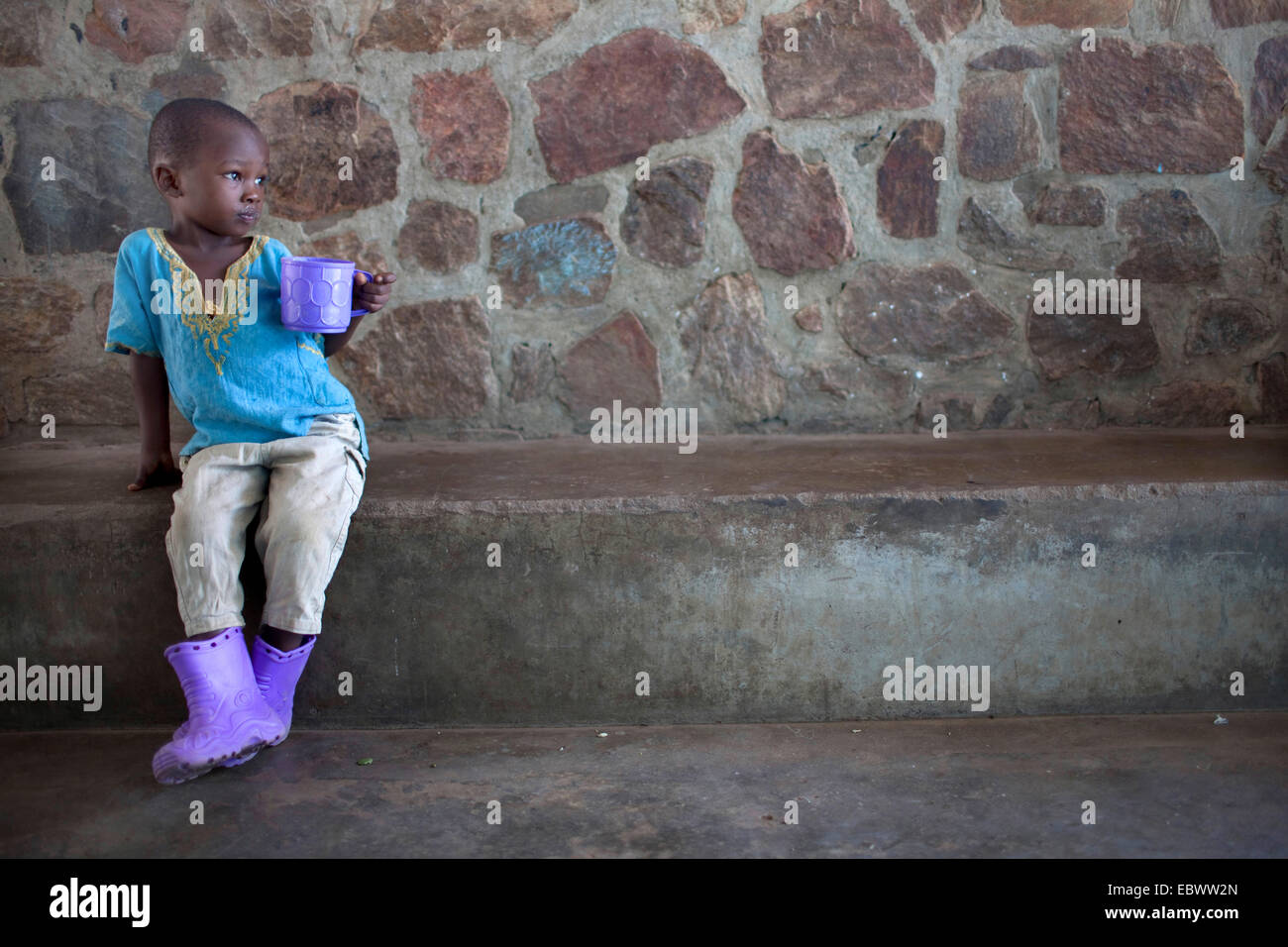 Ragazzino con coppa di porpora viola e stivali di gomma, Burundi Bujumbura Foto Stock
