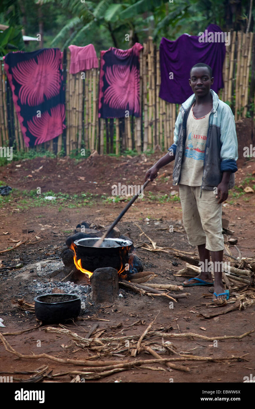 Giovane uomo cucinare un pasto sopra il fuoco sul suolo di terra del cantiere di un ristorante, Burundi, Makamba, Makamba Foto Stock