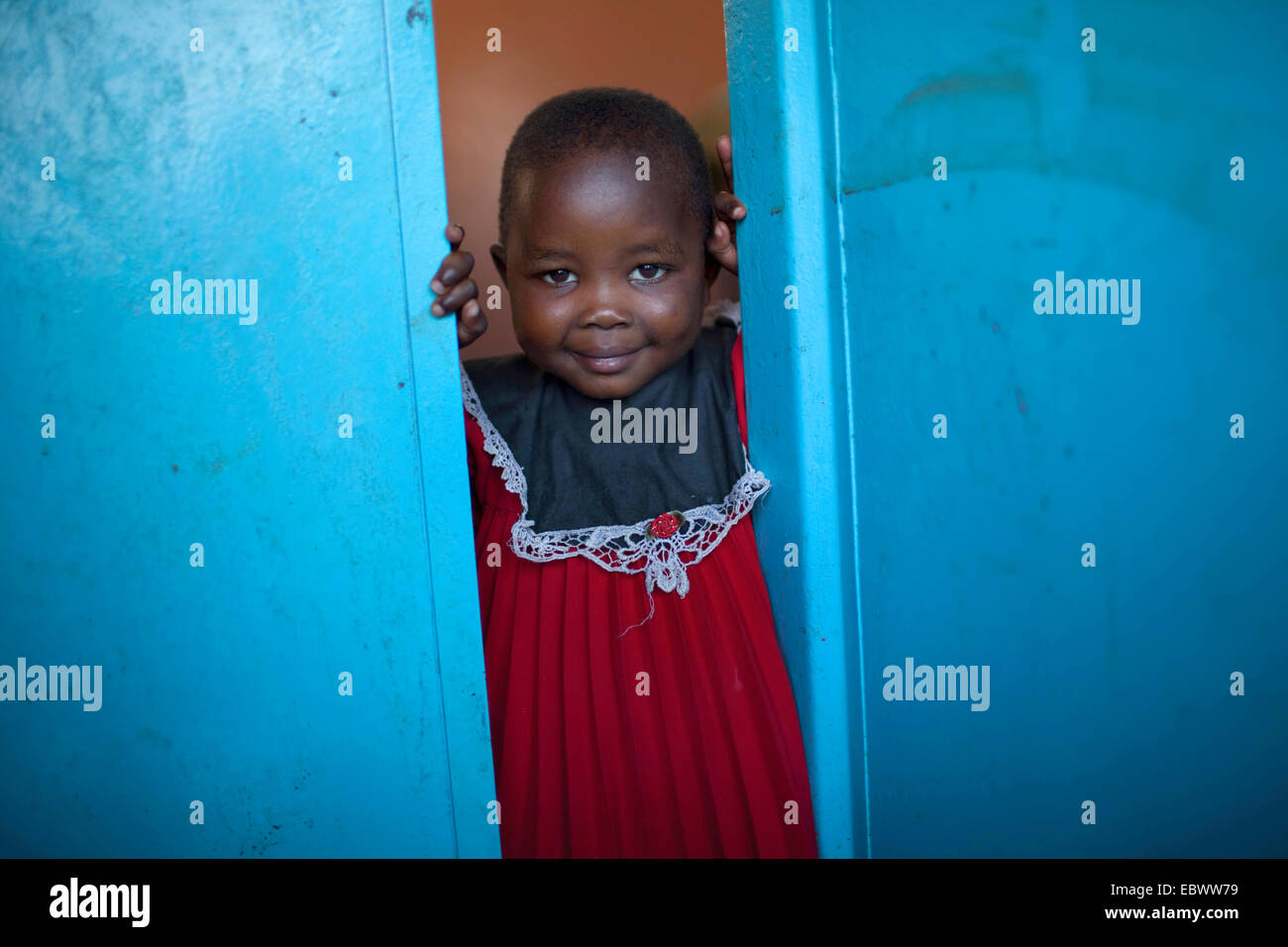 Bambina con un panno rosso guardando fuori da una porta blu, Burundi Bujumbura Mairie, Bujumbura Foto Stock