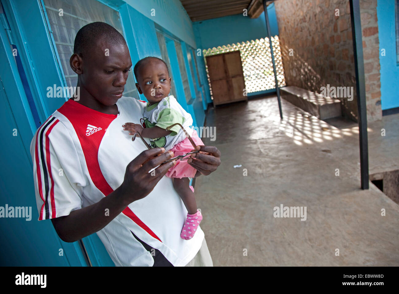 Giovane con un bambino sul suo braccio è in piedi in un corridoio pensieroso guardando i suoi occhiali, Burundi Bujumbura Mairie, Bujumbura Foto Stock