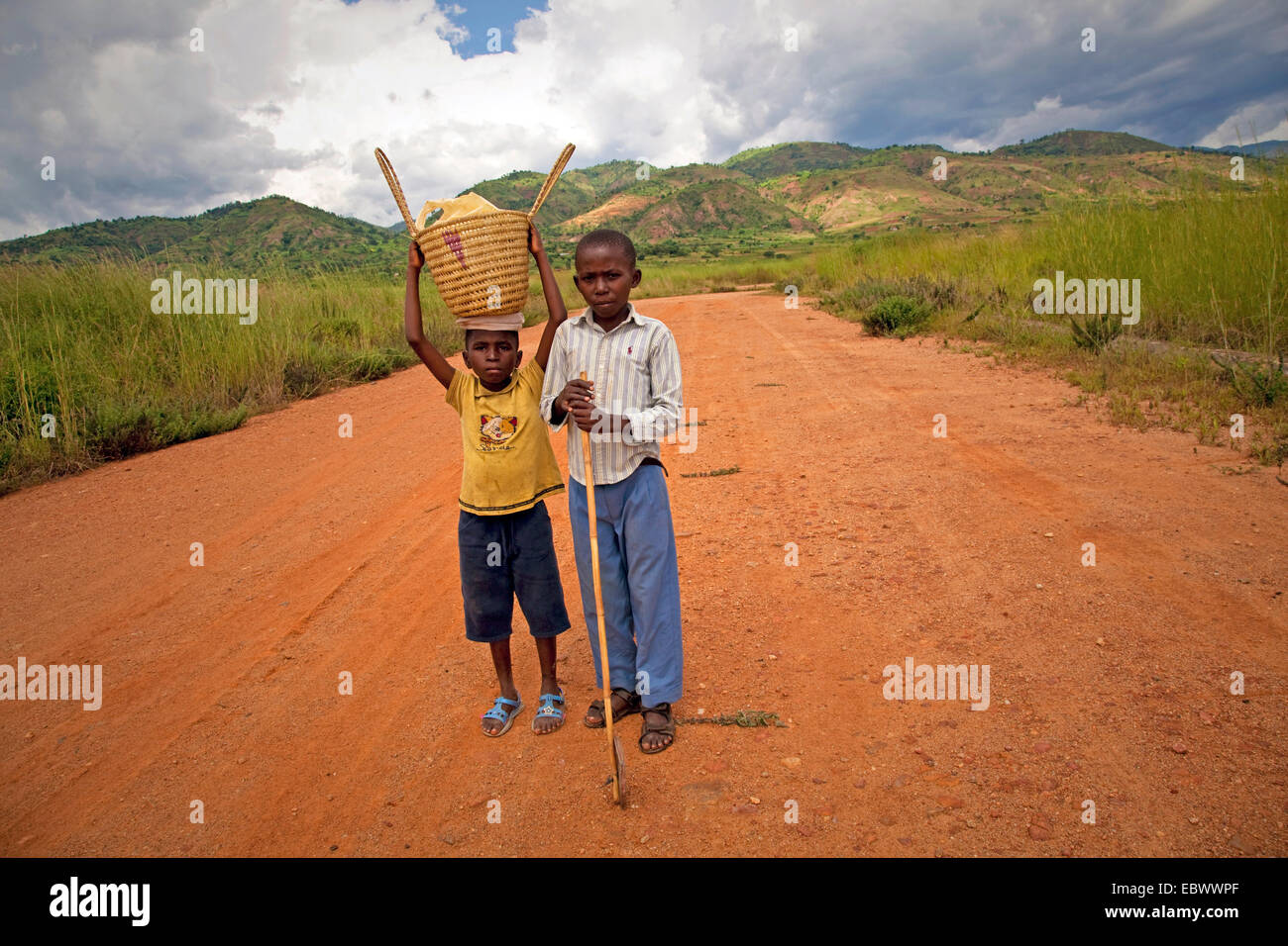 Due ragazzi con cestello e bastone in piedi sul percorso del campo, Burundi Bujumbura Mairie, Bujumbura Foto Stock