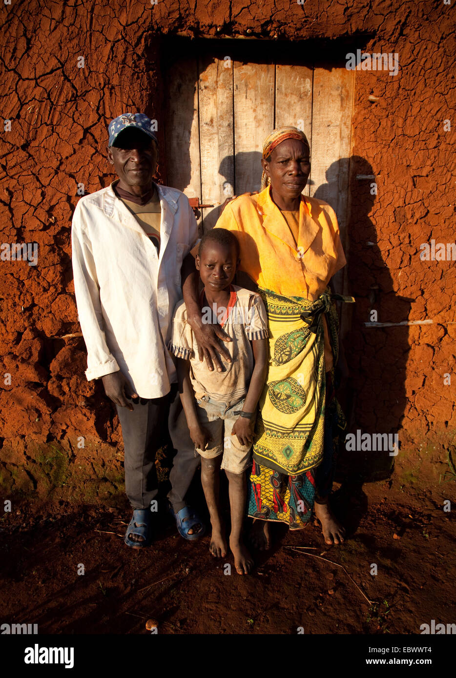 Ritratto di una famiglia di tre persone di fronte alla loro umile casa di fango nella luce del mattino, Burundi, Cankuzo, vicino al Parco Nazionale de la Ruvubu, Cankuzo Foto Stock