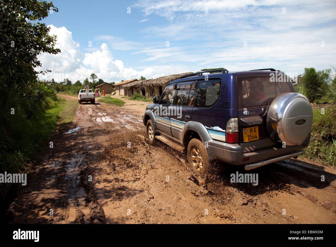 Cross-country veicoli guida attraverso un pozzo del fango su un suolo di strada attraverso la boccola paesaggio passando umili capanne, Burundi, Cankuzo, Nazionale Parc de la Ruvubu, Cankuzo Foto Stock