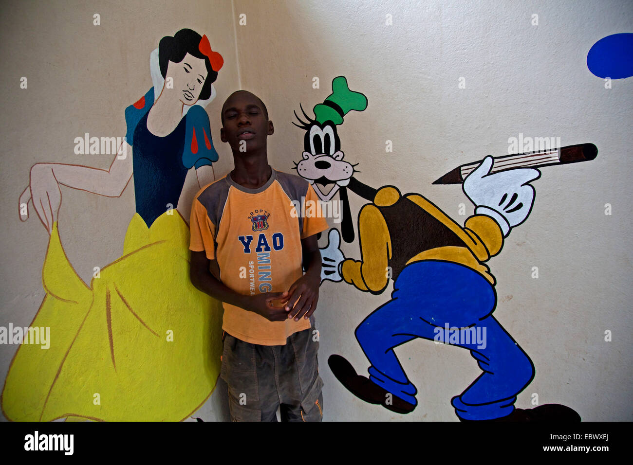 Ragazzo in piedi di fronte ad una parete accanto a Snow White e Pippo dipinto su di esso a sovradimensionare, Burundi Bujumbura Marie, Bujumbura Foto Stock