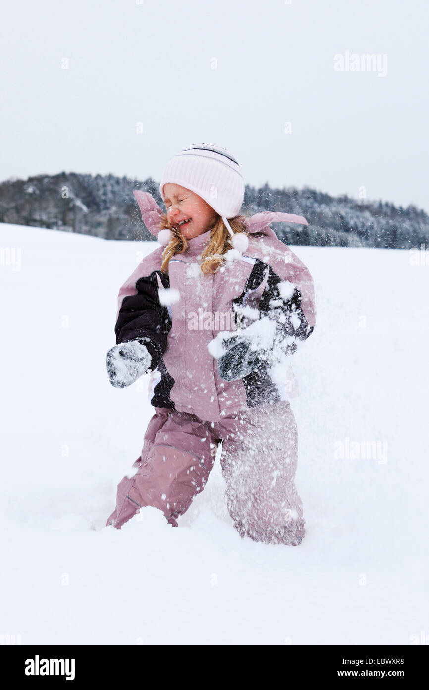 Bambina kneeing nella neve a ridere mentre viene colpito da una palla di neve, Svizzera Foto Stock