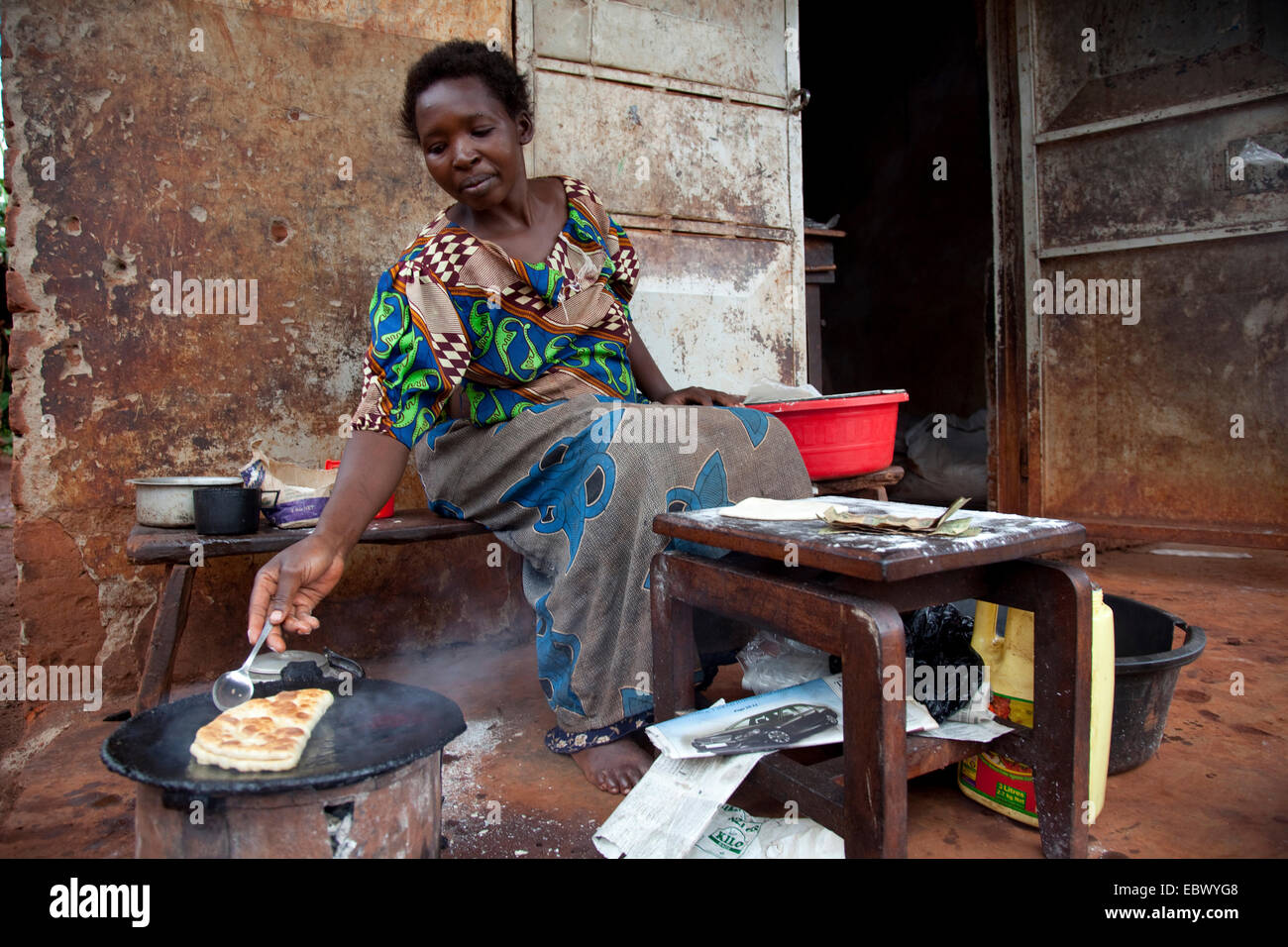La donna è la cottura di un pane chiamato Chapati fatta di farina di mais in un forno charcole davanti a una casa semplice, Uganda Jinja Foto Stock