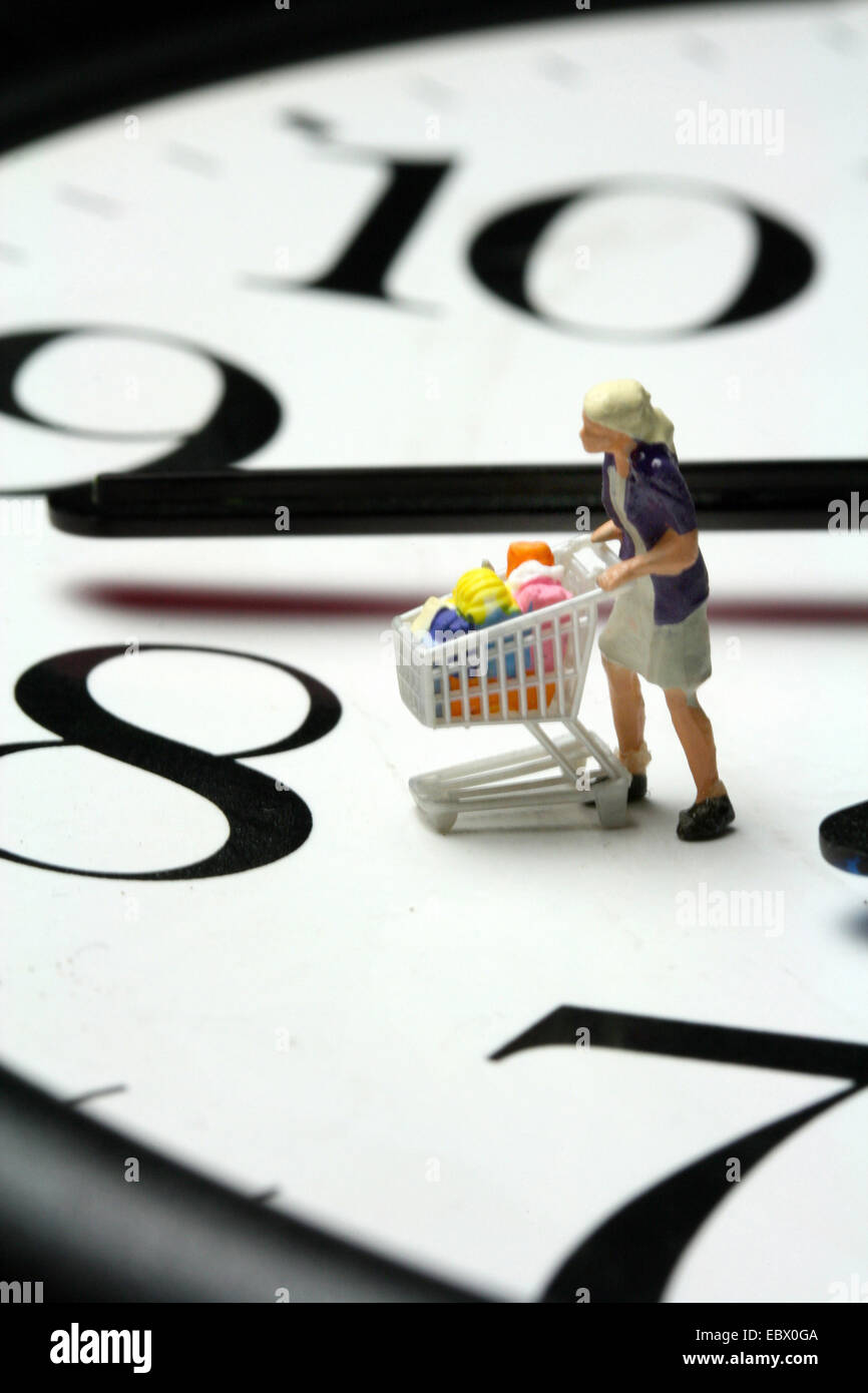Simbolo 'shop ore": il personaggio giocattolo di una giovane donna su un orologio spingendo un intero carrello della spesa Foto Stock