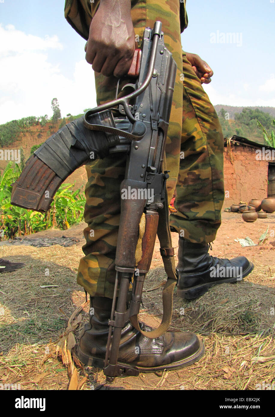 Le gambe di un soldato con la pistola in piedi di fronte a una casa di fango, Burundi Bujumbura rurale, Mutimbuzi Foto Stock