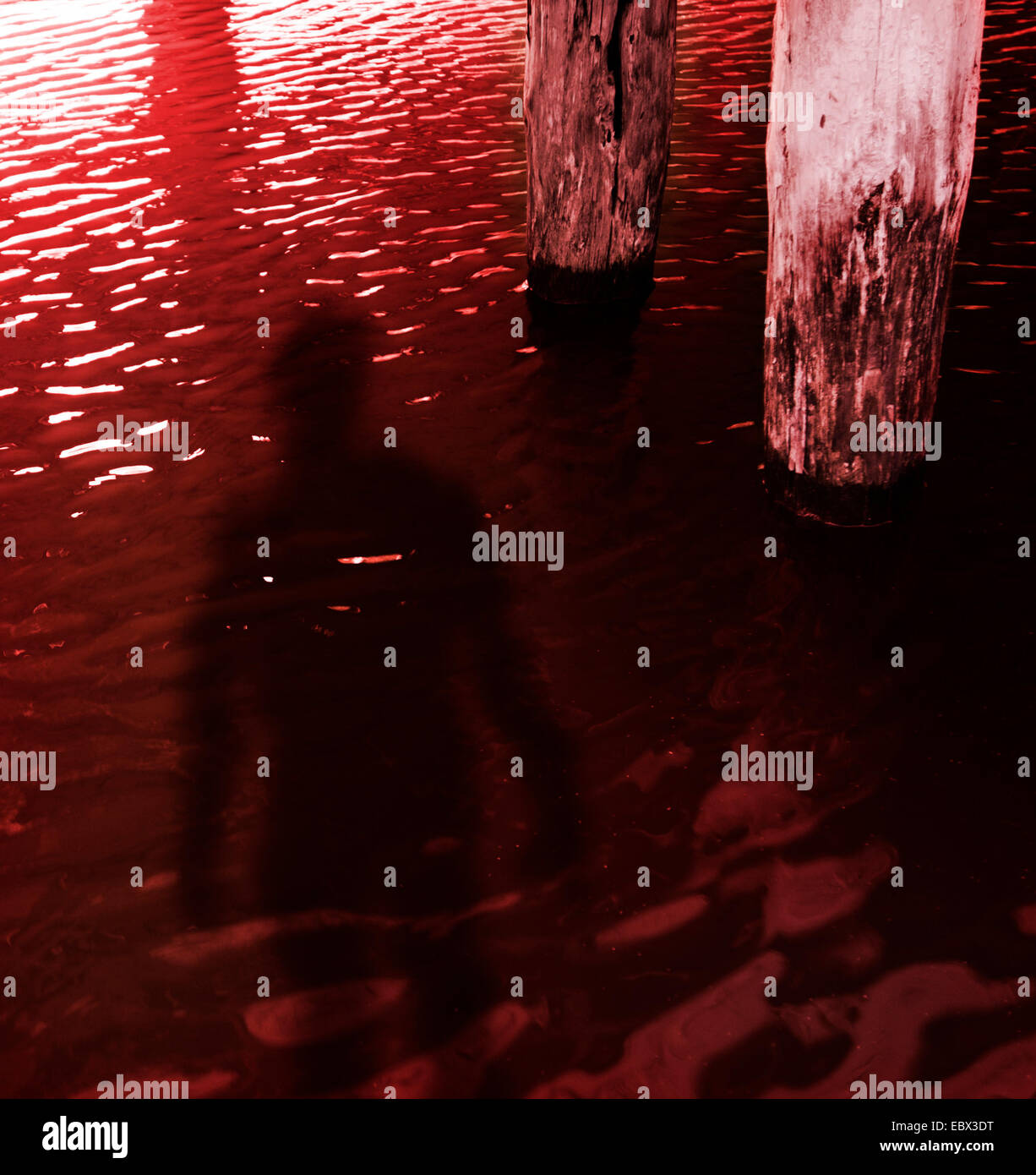 Oscuro presagio di persona in rosso acqua sotto un molo Foto Stock