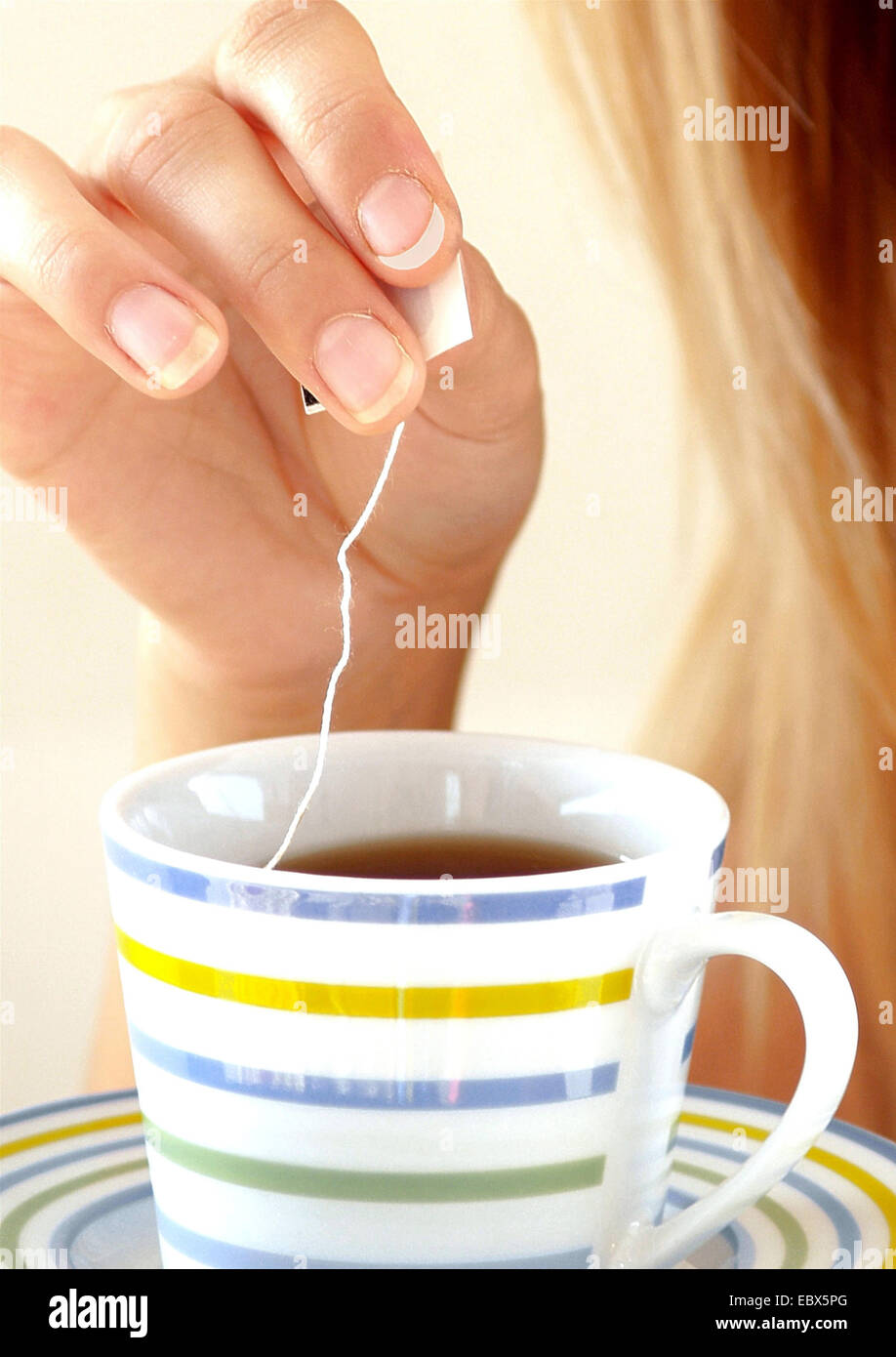 Con i capelli lunghi giovane donna bionda immergendo un sacchetto da tè in una tazza Foto Stock