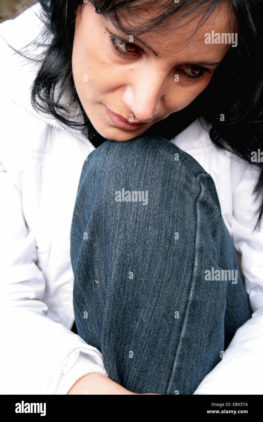 Yioung donna seduta con la testa appoggiata su un ginocchio perso nel pensiero Foto Stock