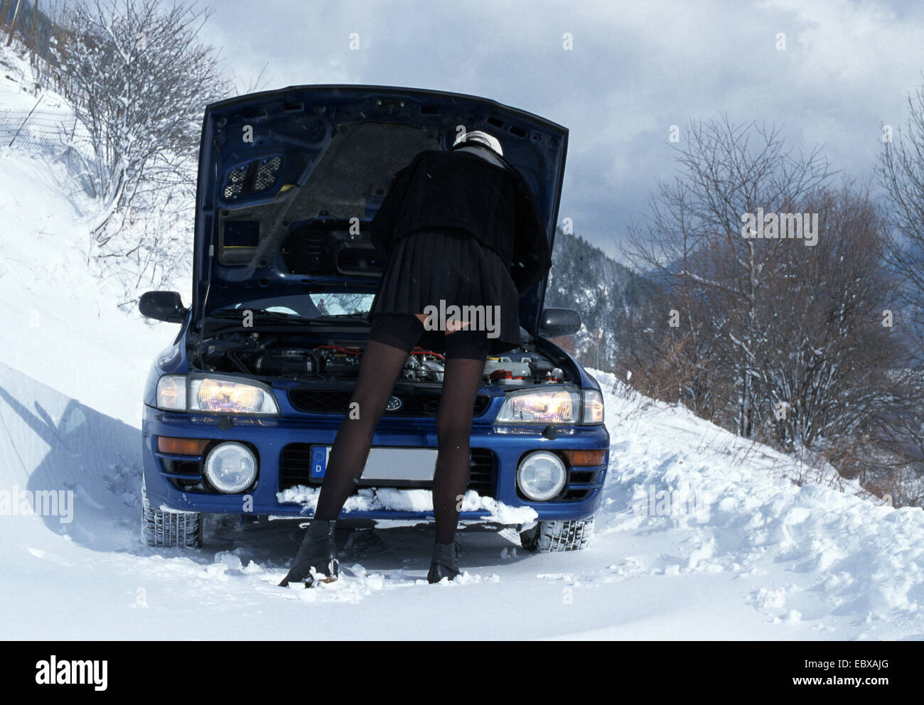 Donna che indossa minigonna e calze autoreggenti riparazione auto nel paesaggio invernale Foto Stock