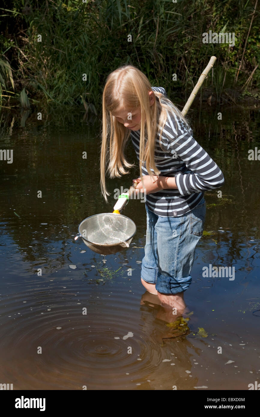Ragazza con un dip selfmade net, fatta da uno scolapasta, stando in piedi in un torrente Foto Stock