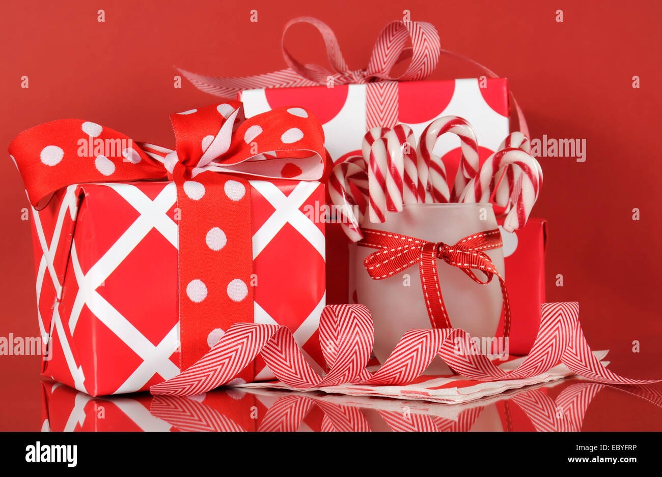 Pila di luminosi rosso e bianco polka dot e controllare la festa di Natale confezioni regalo su sfondo rosso, con stripe canne di caramella. Foto Stock