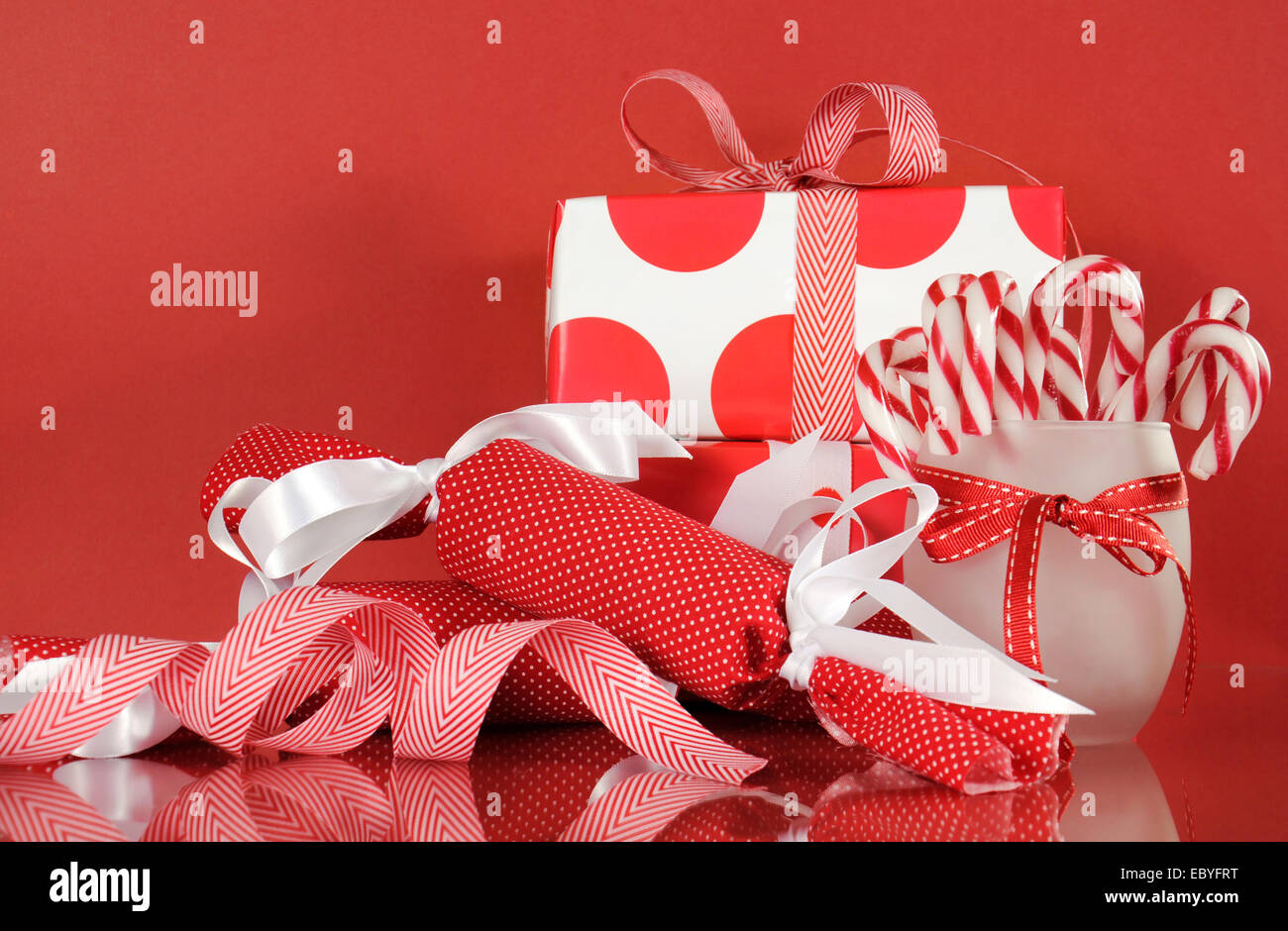 Pila di luminosi rosso e bianco polka dot e controllare la festa di Natale confezioni regalo su sfondo rosso, con stripe candy canes Foto Stock