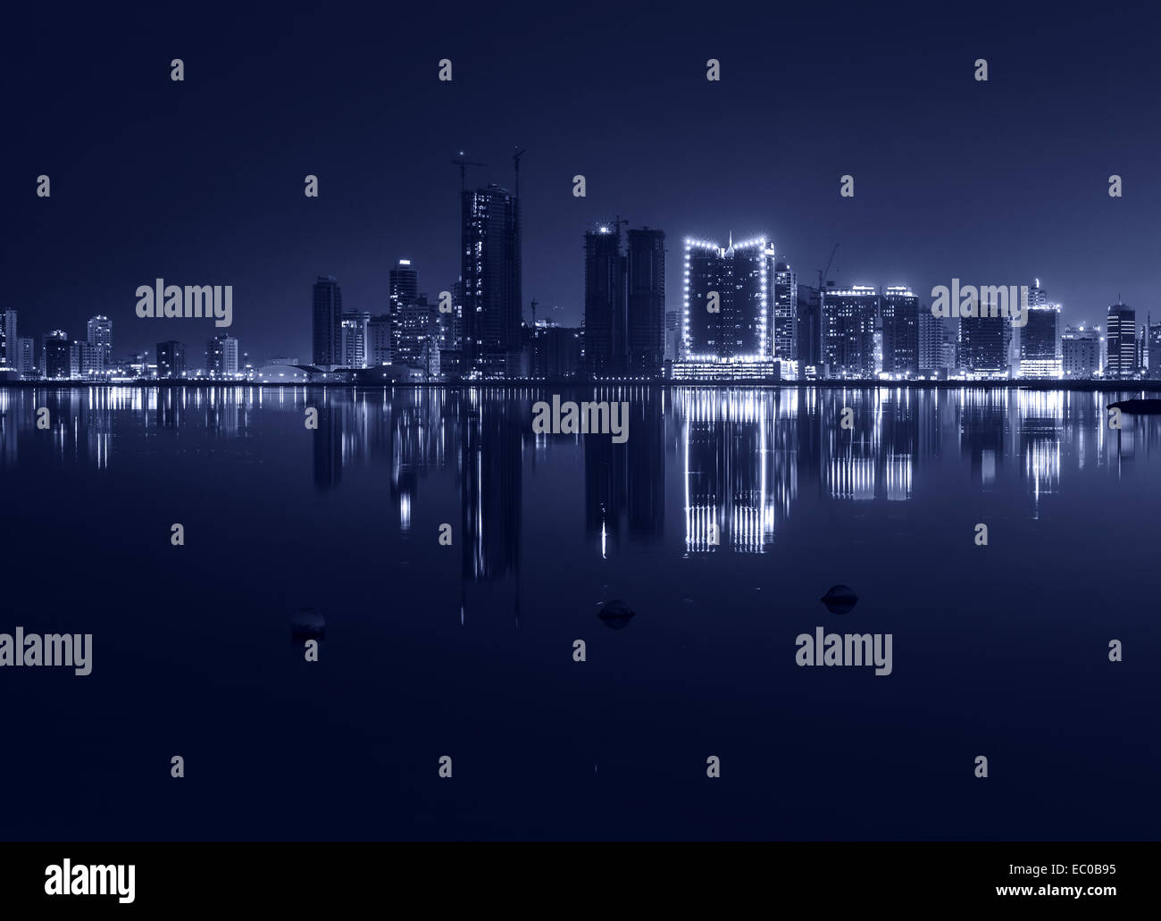 Notte moderno skyline della città con brillanti luci e riflesso nell'acqua. Manama, la capitale del Bahrein, Medio Oriente. Monochro Foto Stock