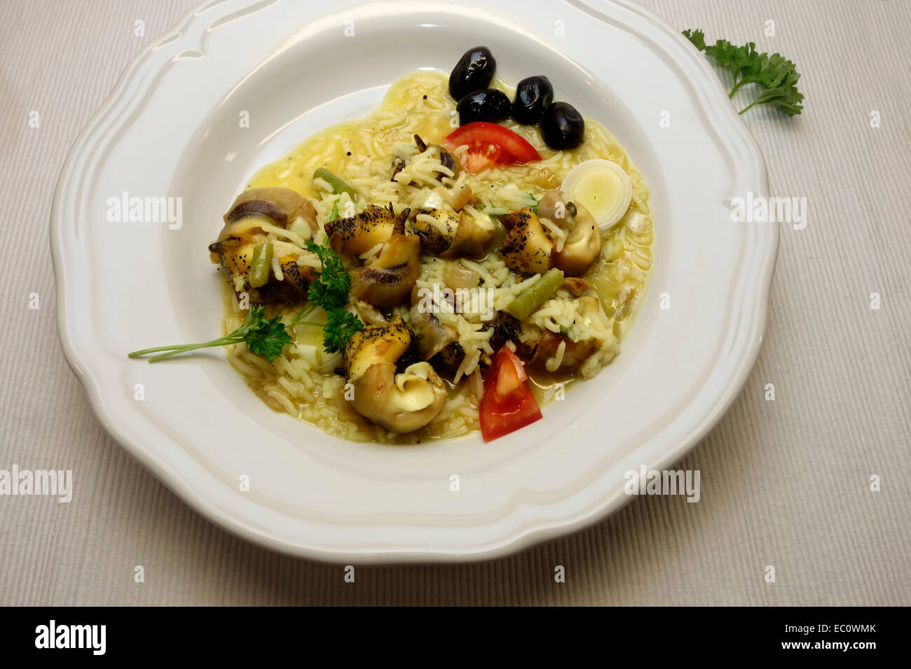 Risotto con carne di conchiglia servita su piastra bianca con aggiunta di olive nere e pomodoro. Foto Stock