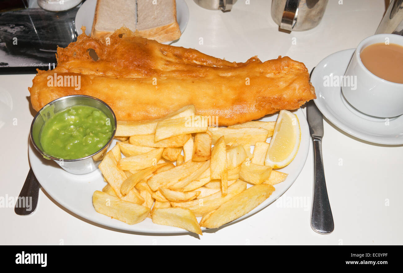 Piatto di pesce e patatine fritte con fiacco piselli, il pane e la tazza di tè. Foto Stock