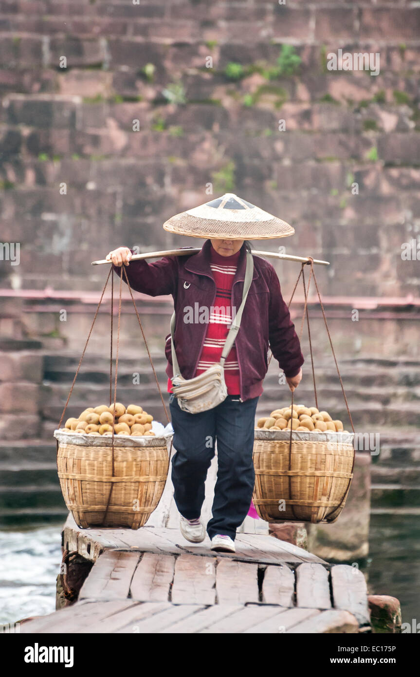 Donna locale portando cesti di frutta attraverso un ponte di legno, Fenghuang, Cina Foto Stock
