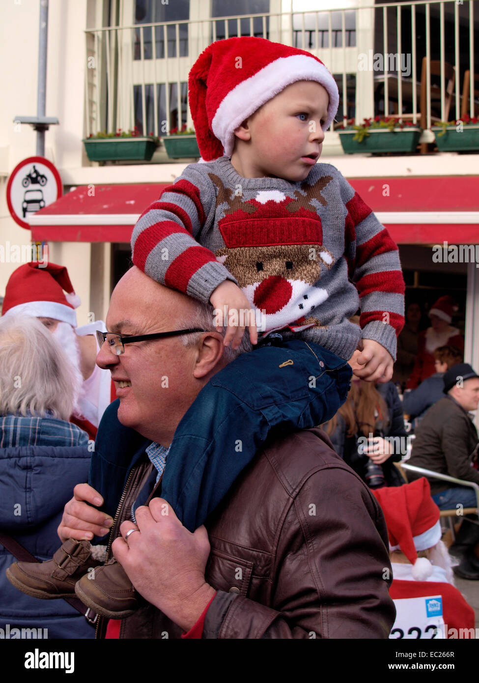 Il nonno che porta il bambino che indossa un ponticello di Natale e hat sulle sue spalle, Padstow, Cornwall, Regno Unito Foto Stock