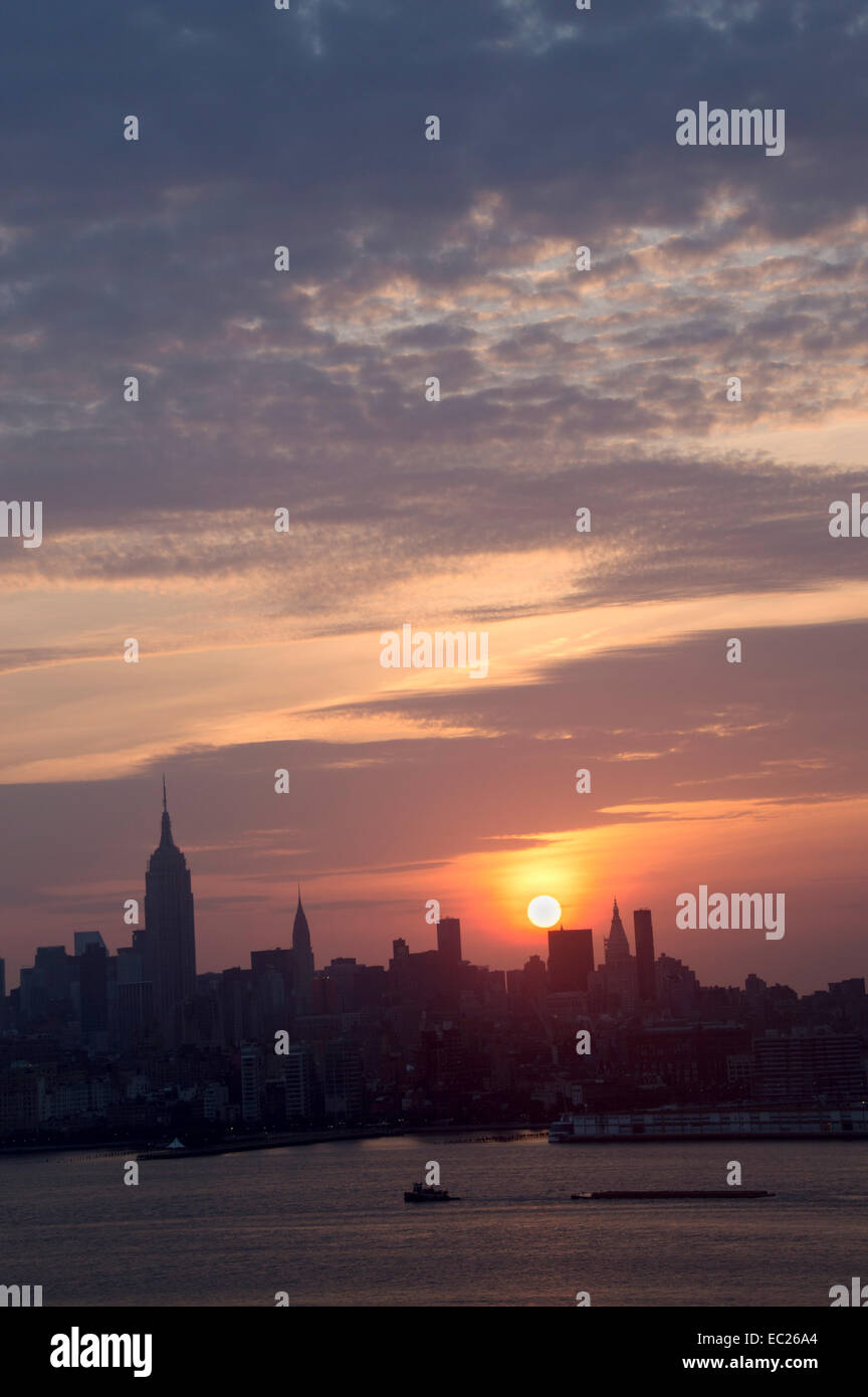 Sole sorge su Manhattan, scontornamento l'isola, come barche di iniziare la loro mattina commutare sul fiume Hudson. Foto Stock