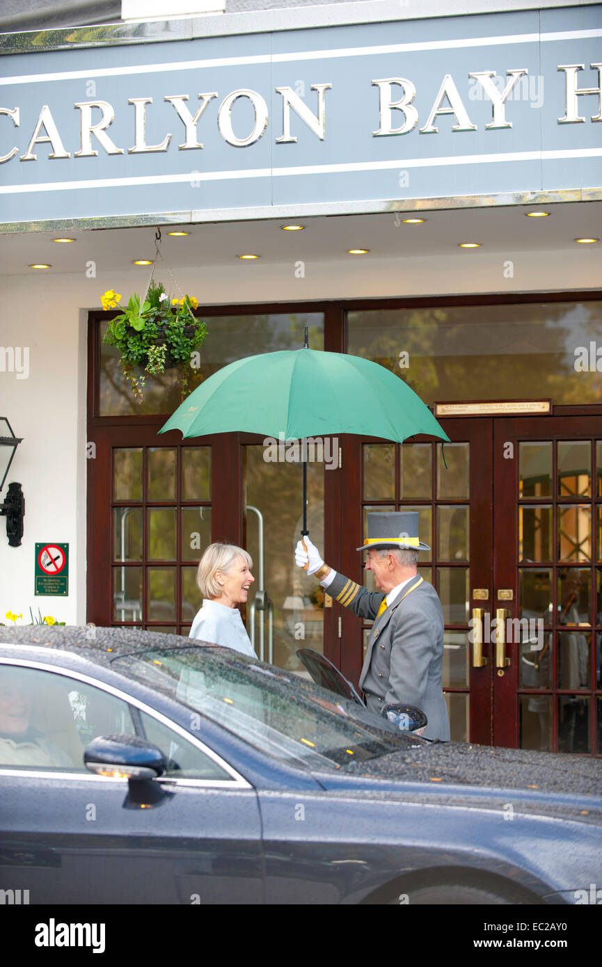 Un portiere con ombrello per una valutazione al di fuori di un ingresso in hotel Foto Stock