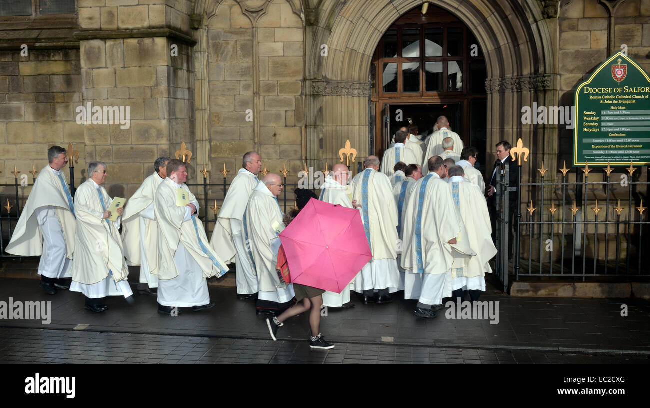 Salford, Greater Manchester, UK 8 dicembre 2014 una giovane donna che porta un ombrello rosa passeggiate passato come sacerdoti della diocesi Cattolica Romana di Salford entrare nella Cattedrale per la solenne Messa di installazione di destra il Reverendo John Stanley Kenneth Arnold come l'undicesimo vescovo di Salford. Egli sostituisce il vescovo Terence cervello, che si è ritirato dopo essere diventato il decimo vescovo nel 1997. Il vescovo Arnold era precedentemente un vescovo ausiliare della diocesi di Westminster. Nuovo vescovo romano cattolico di Salford Credito: Giovanni friggitrice/Alamy Live News Foto Stock