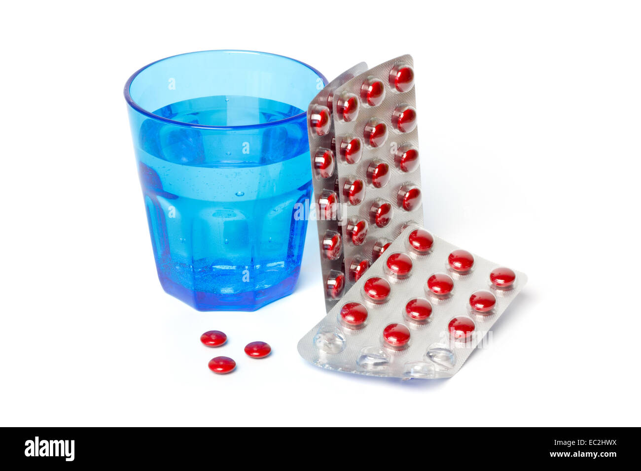 Strisce di pillole e un vetro blu con acqua contro uno sfondo bianco Foto Stock