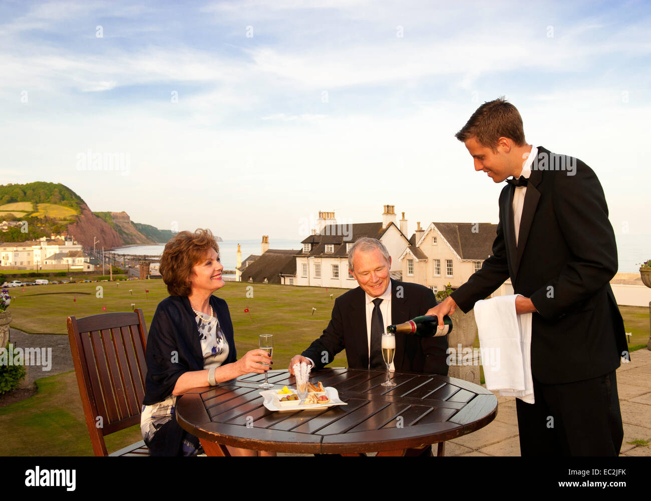 Una coppia di anziani di essere servito champagne all'aperto presso un hotel sulla costa sud del Devon Foto Stock