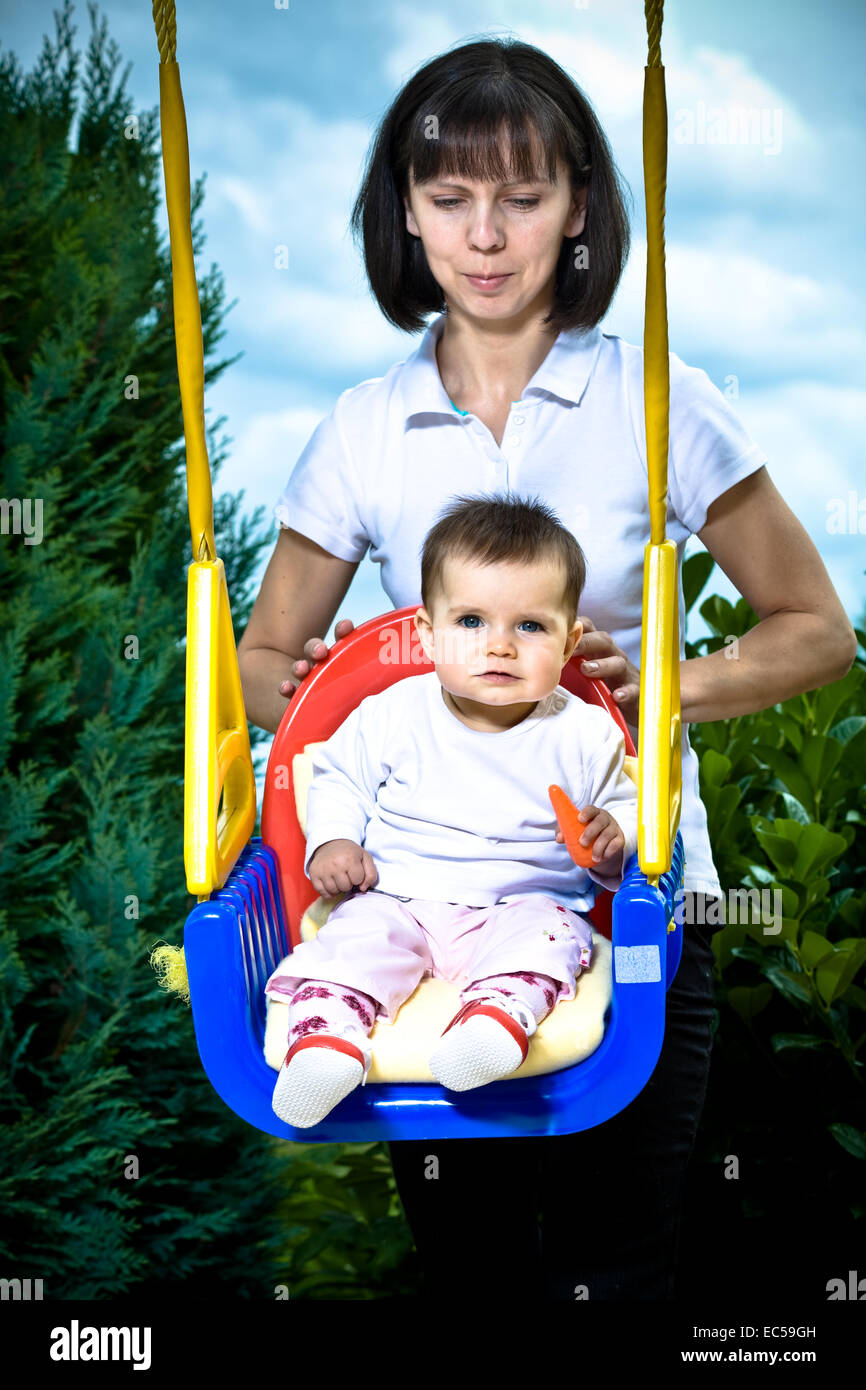 Un 8 mese vecchia ragazza oscillante con mamma in giardino Foto Stock