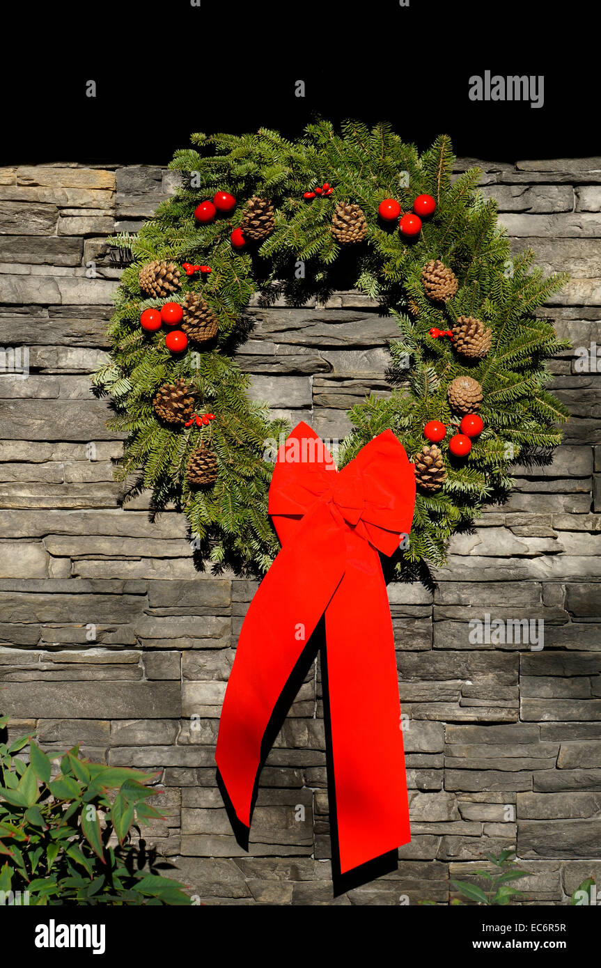 Ghirlanda di Natale con pigne e grande arco rosso appeso ad un muro di pietra naturale Foto Stock