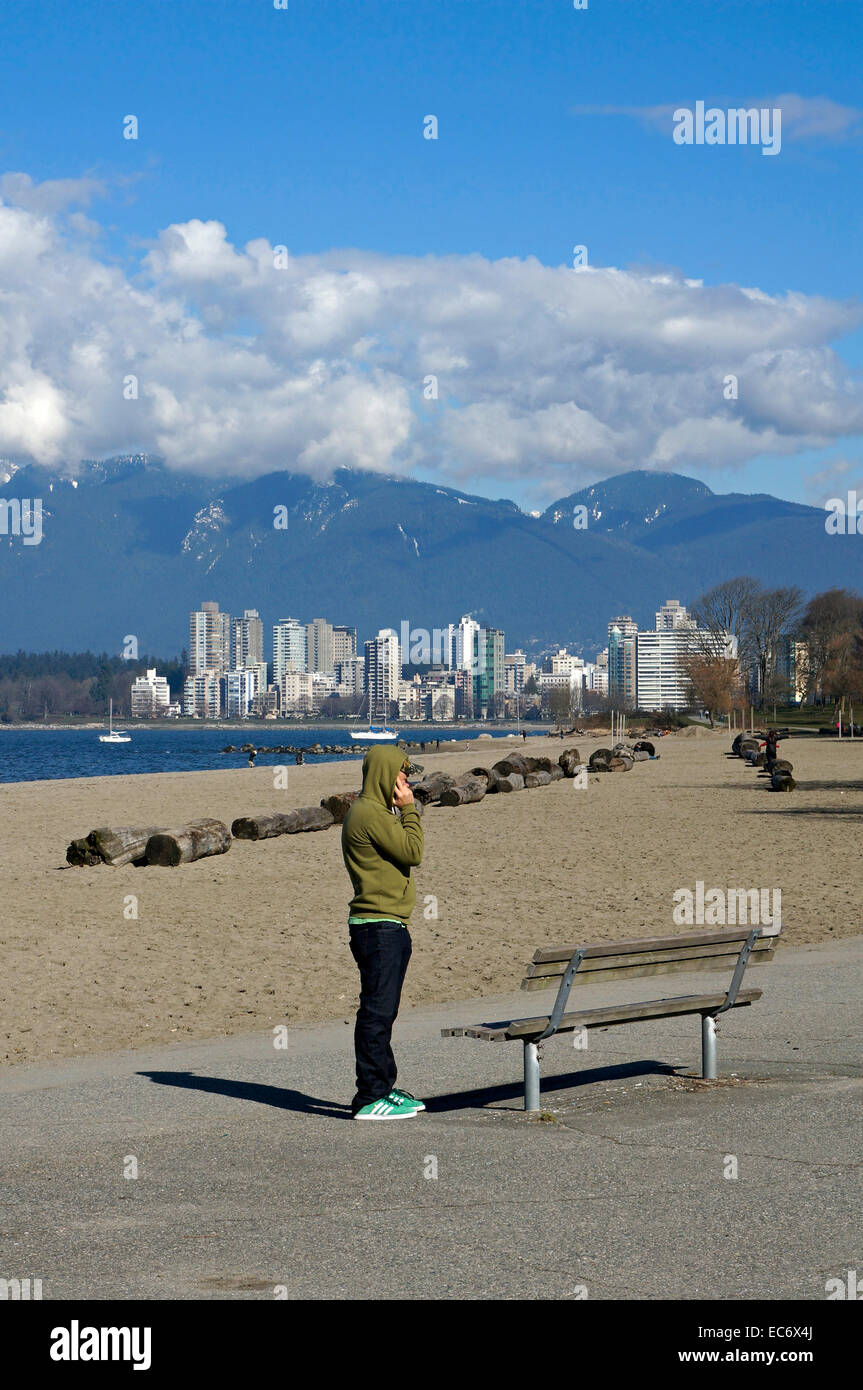 Giovane uomo che indossa una felpa con cappuccio a parlare su un telefono cellulare sulla spiaggia Kit, Kitsilano, Vancouver, BC, Canada Foto Stock