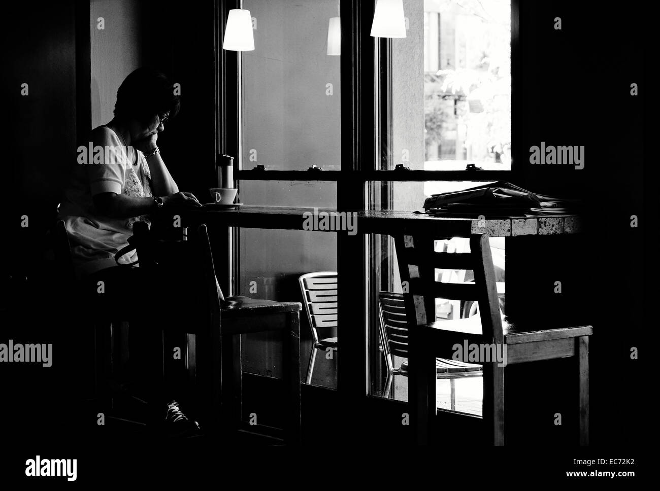 Moody alto contrasto immagine in bianco e nero di una donna di mezza età seduta accanto alla finestra in una caffetteria Foto Stock