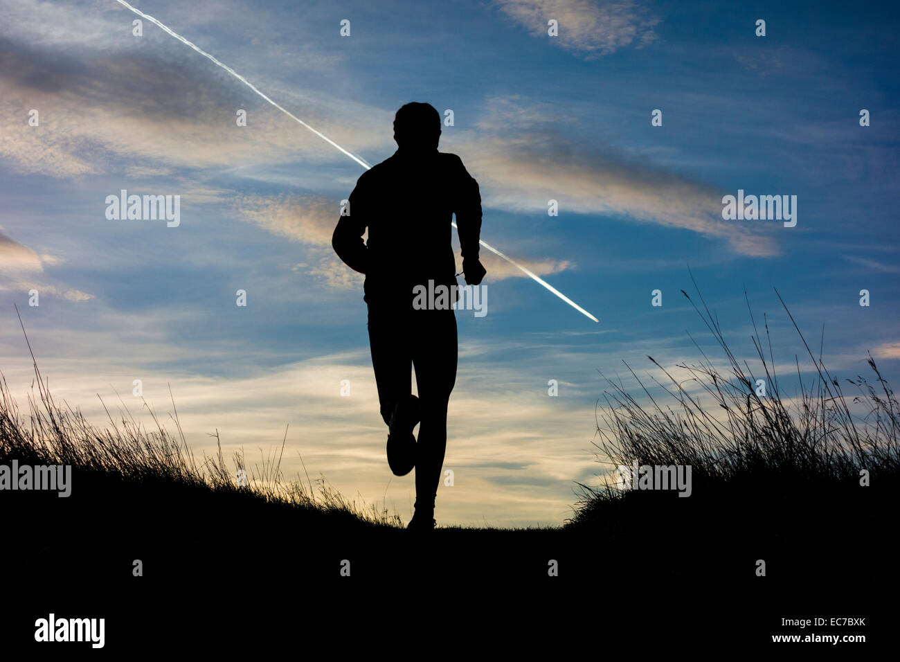 L'uomo jogging in salita sul sentiero del paese stagliano contro Alba cielo a sunrise Foto Stock