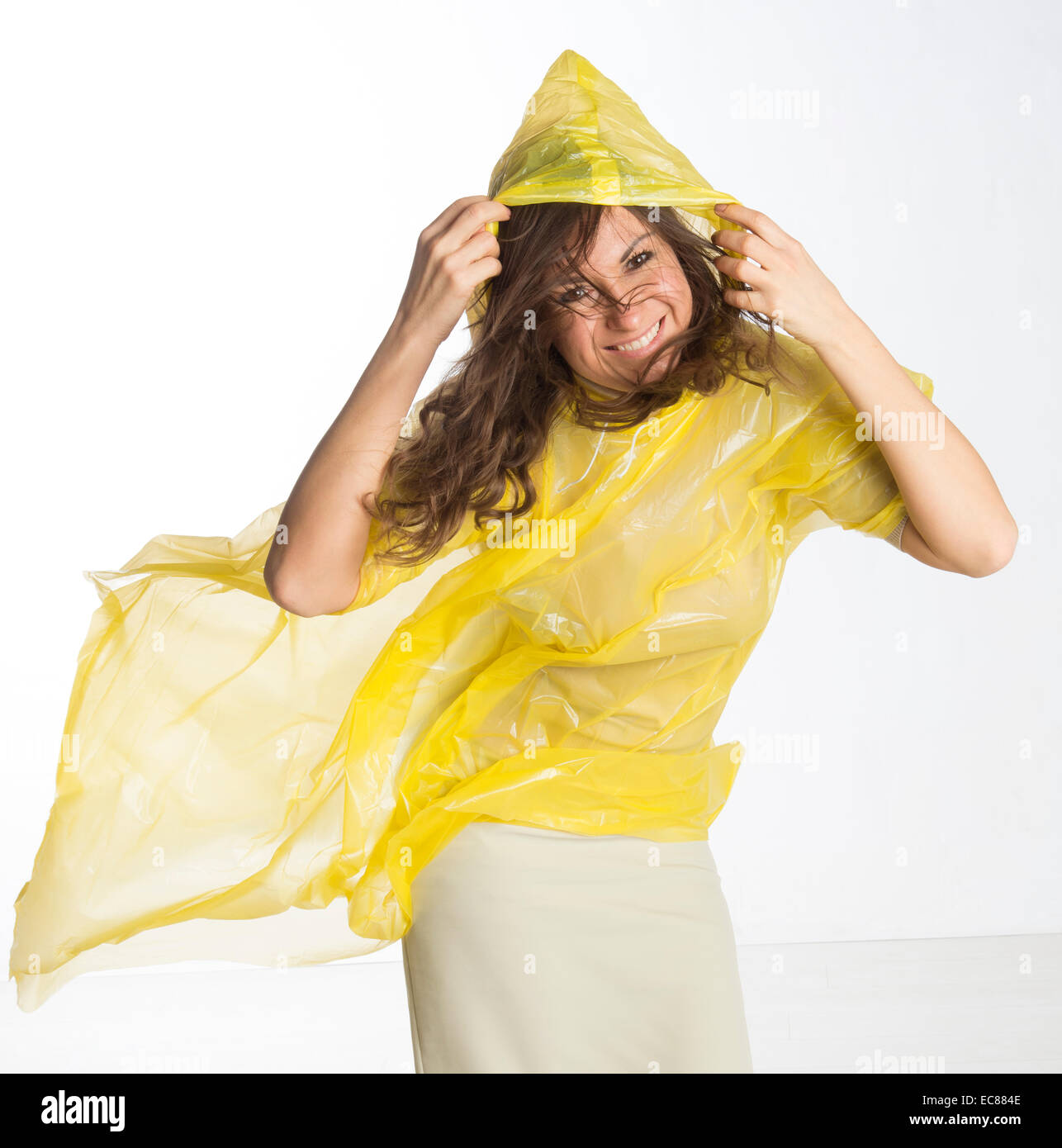 Donna che indossa un giallo poncho di plastica e trattenere il cofano in umidità condizioni ventose Foto Stock