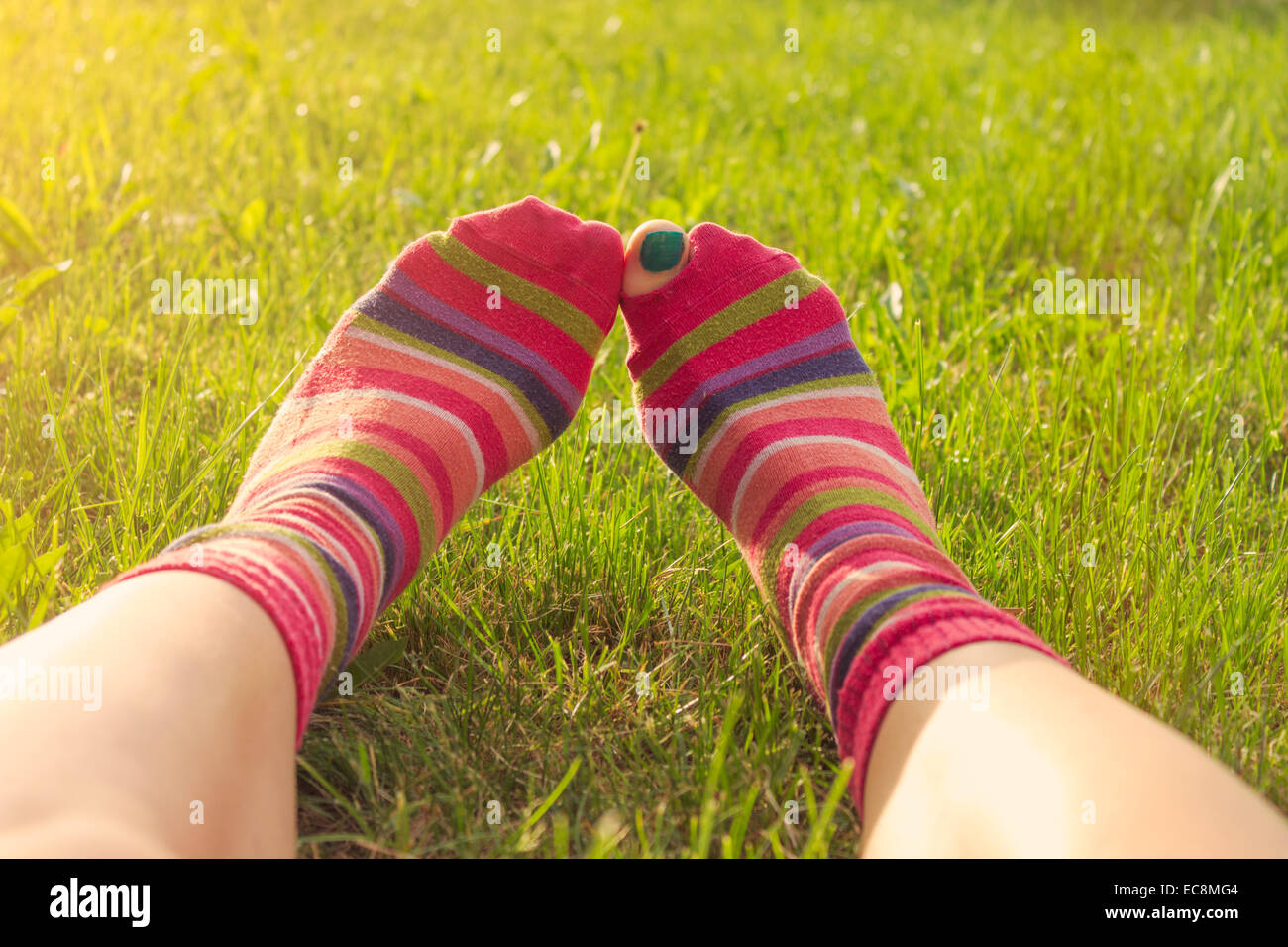 Ragazza adolescente godendo la molla giacente in erba, piedi in strappata calze colorate, toe peeping. Punto di vista personale, lens flare Foto Stock